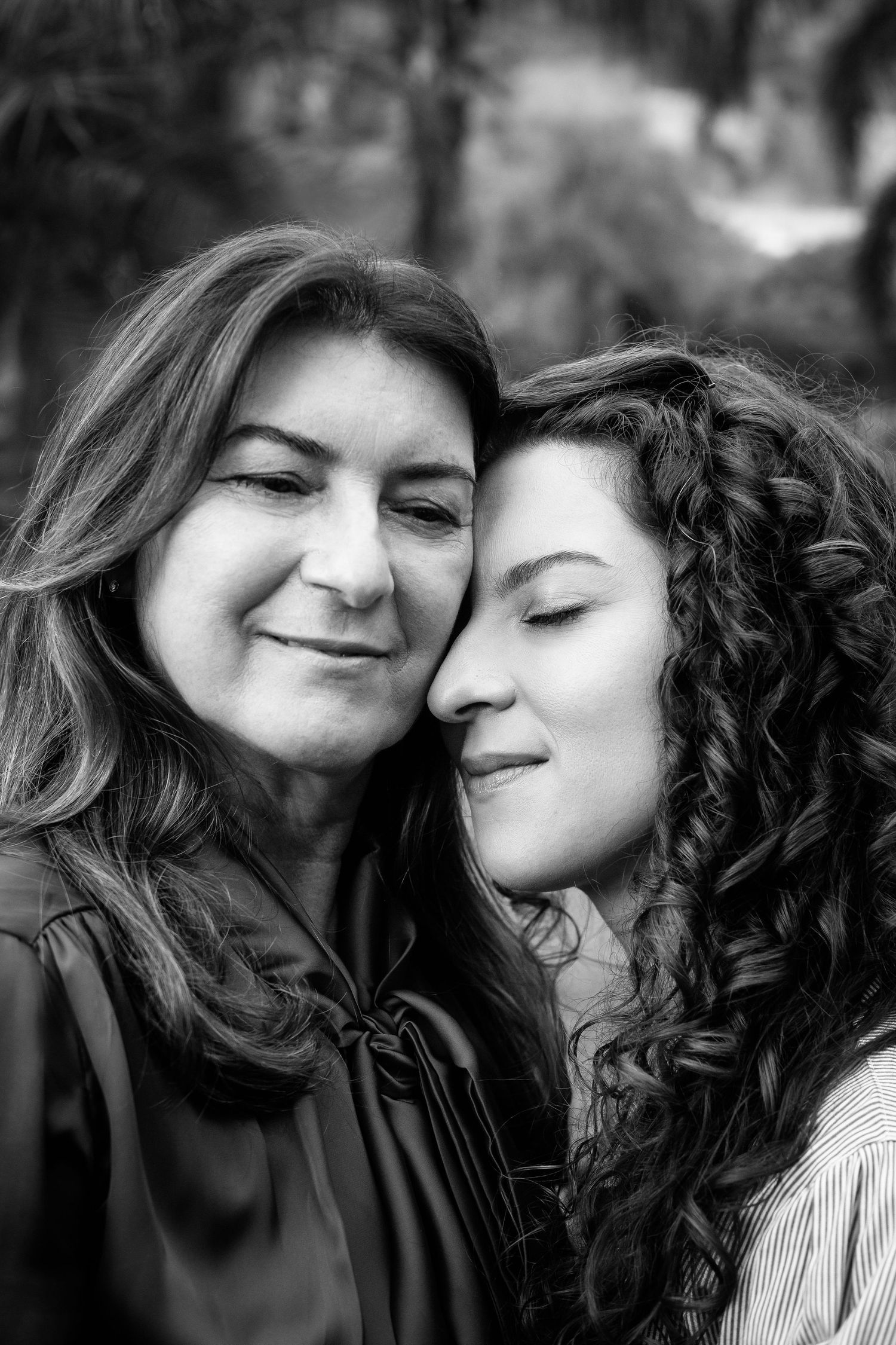 An intimate black and white portrait showing two people in a close embrace outdoors.