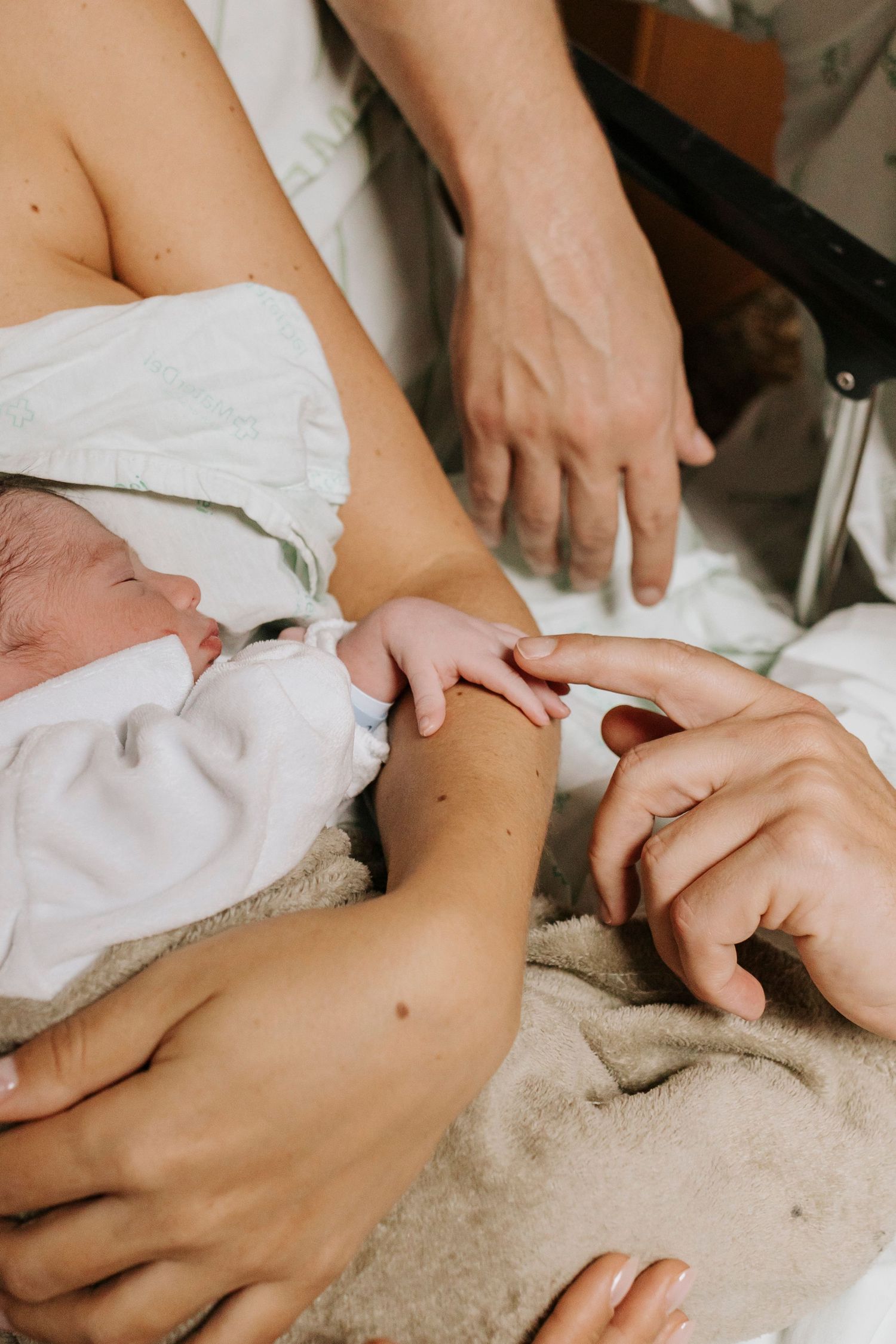 Close-up shot of gentle hands holding newborn baby wrapped in hospital blanket.