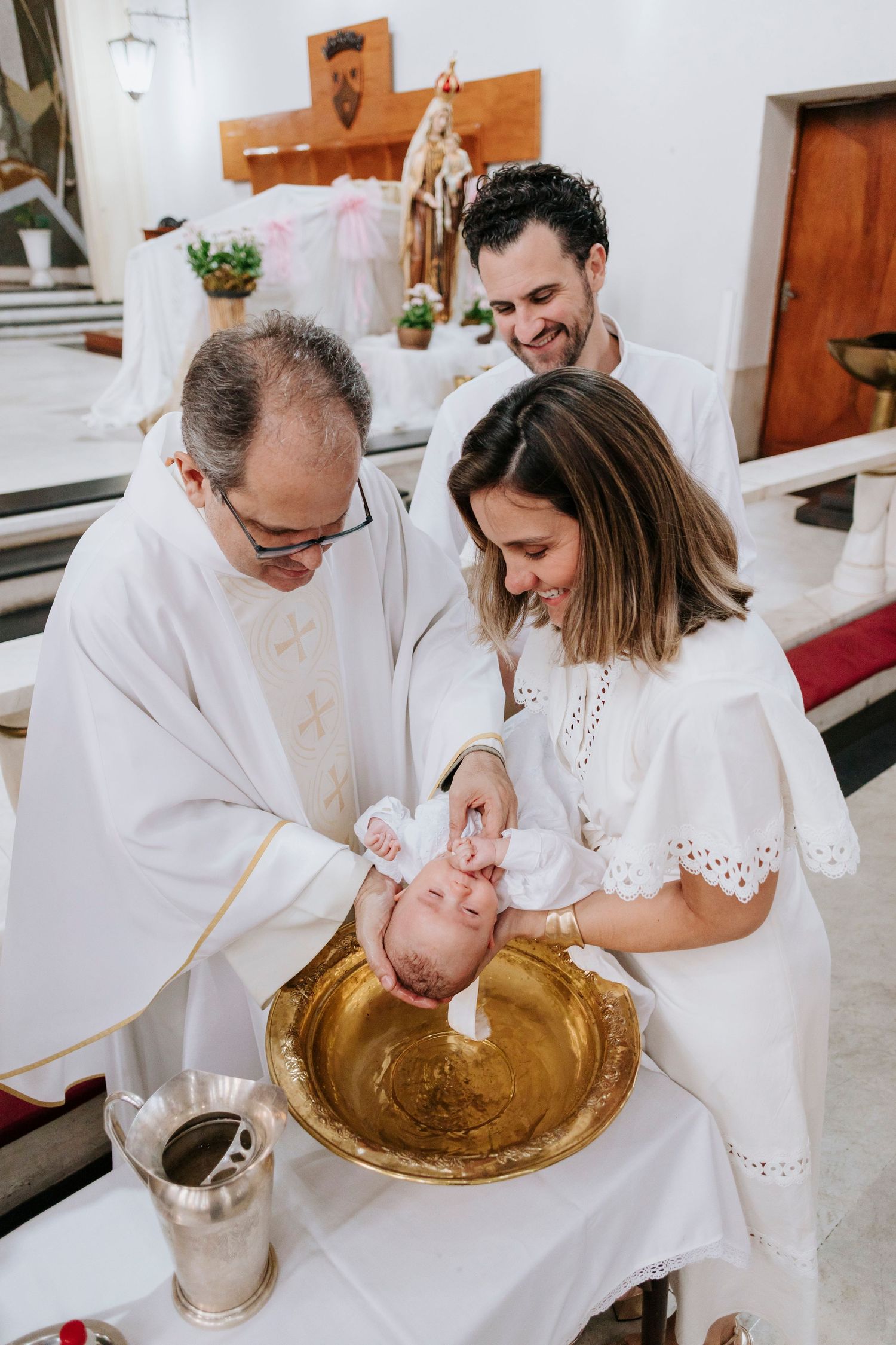 A baptism ceremony takes place in a church as a priest performs the ritual over an infant in a golden basin.