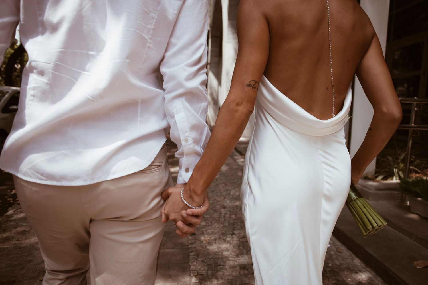 Couple in white wedding attire holding hands in an intimate moment during their special day.