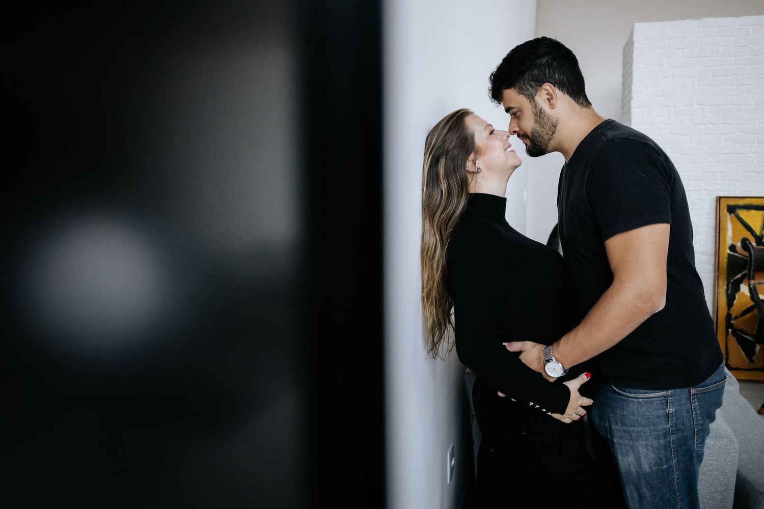 Expecting couple shares intimate moment in contemporary room with natural lighting.