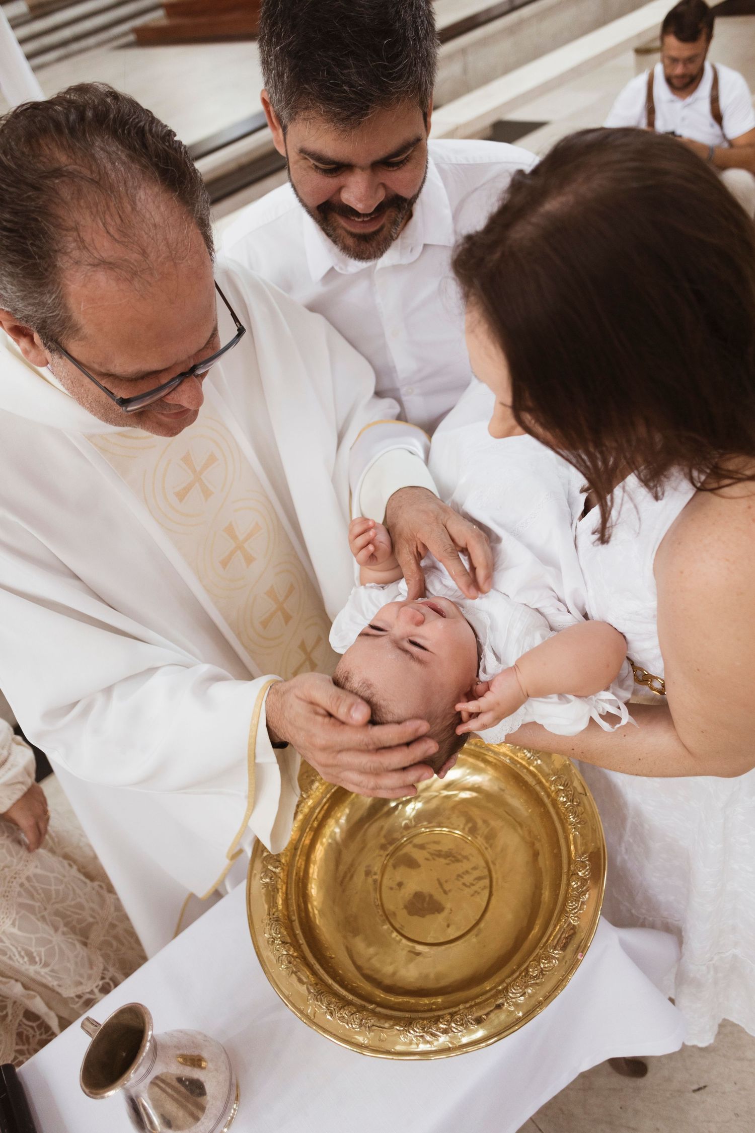 Priest and parents perform baptism ritual over golden basin in church.