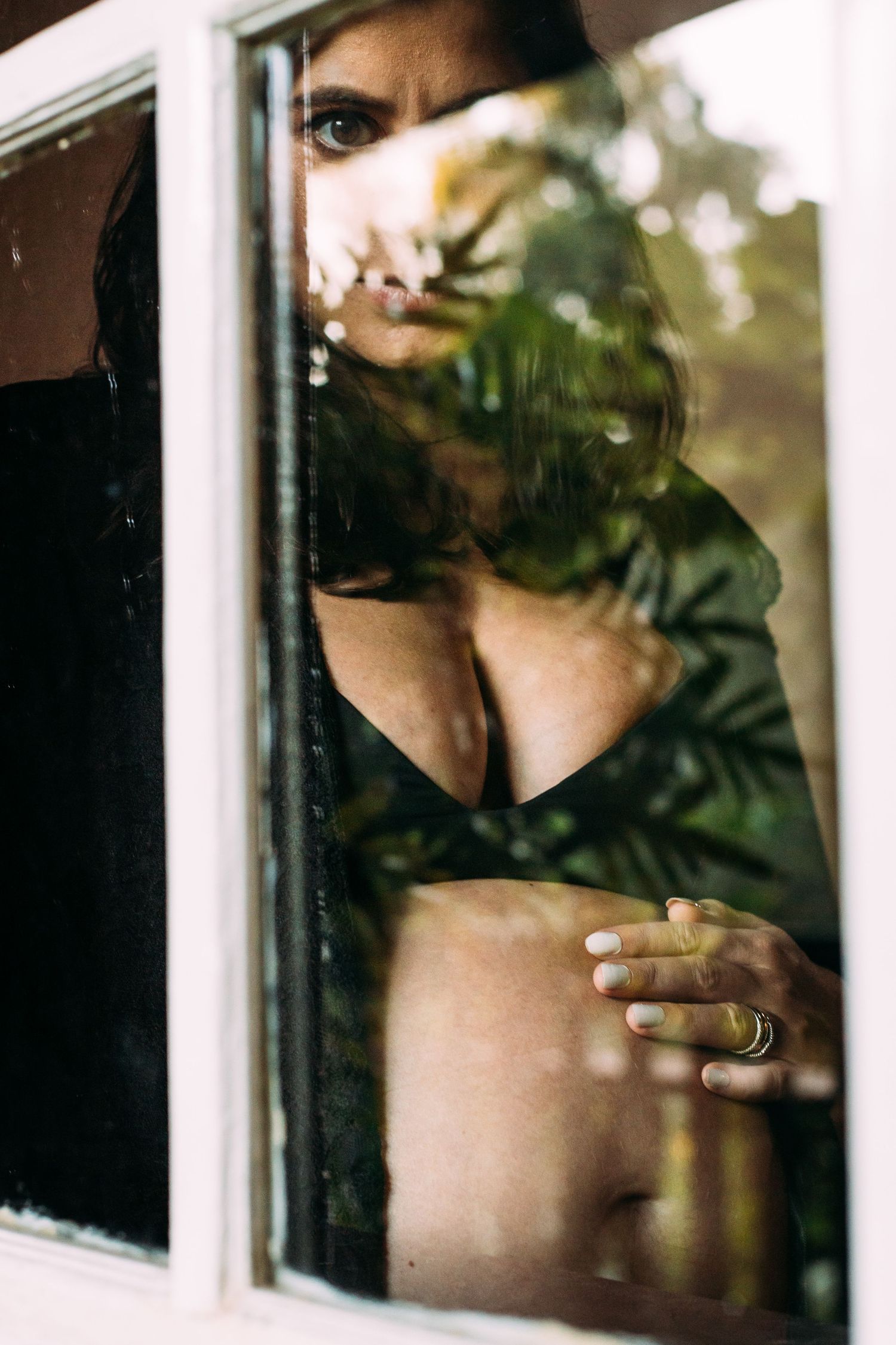 Art series captures intimate figure through window frame with reflections and shadows on glass.