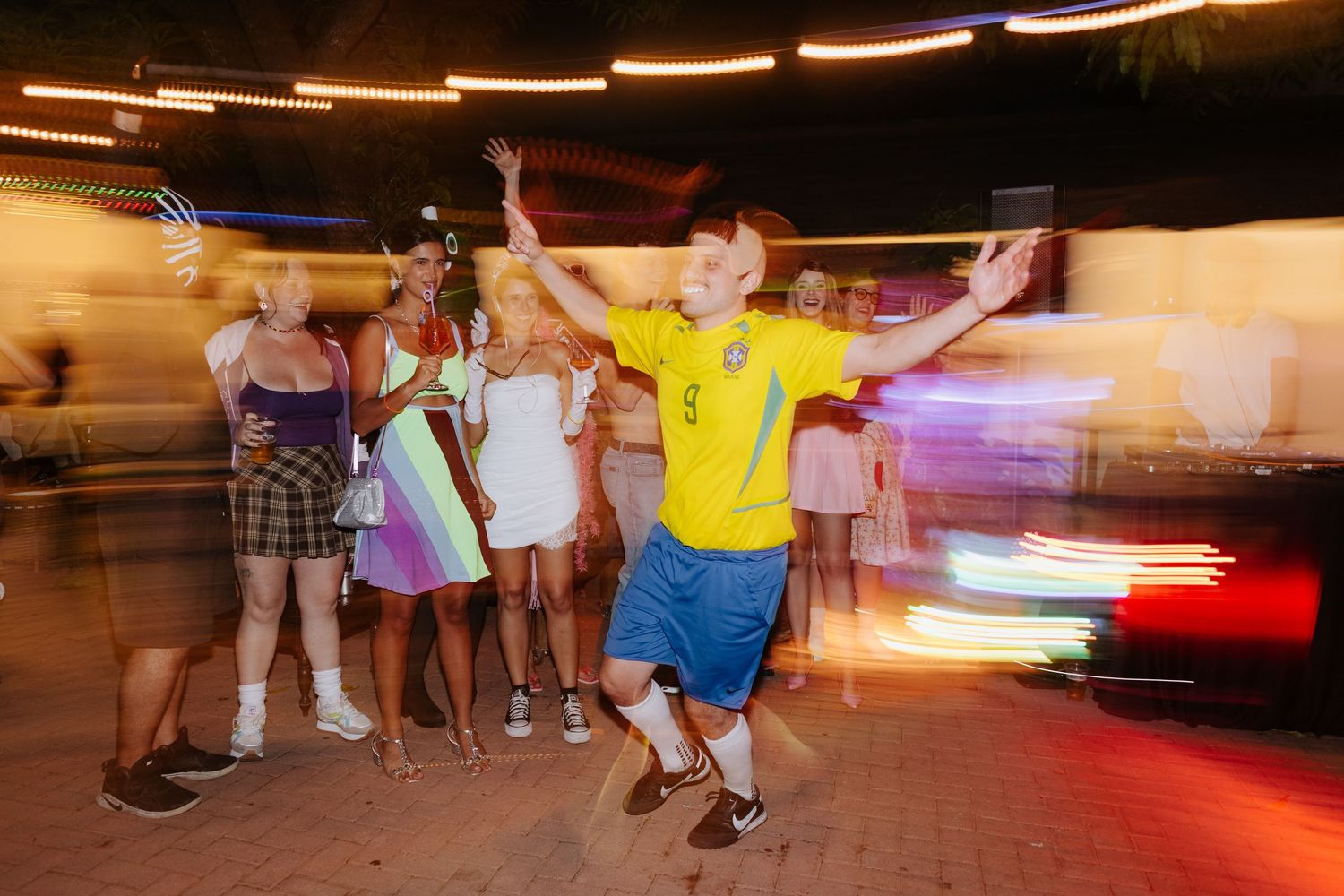 People dancing and moving in a dimly lit venue with streaks of light creating motion blur effects.