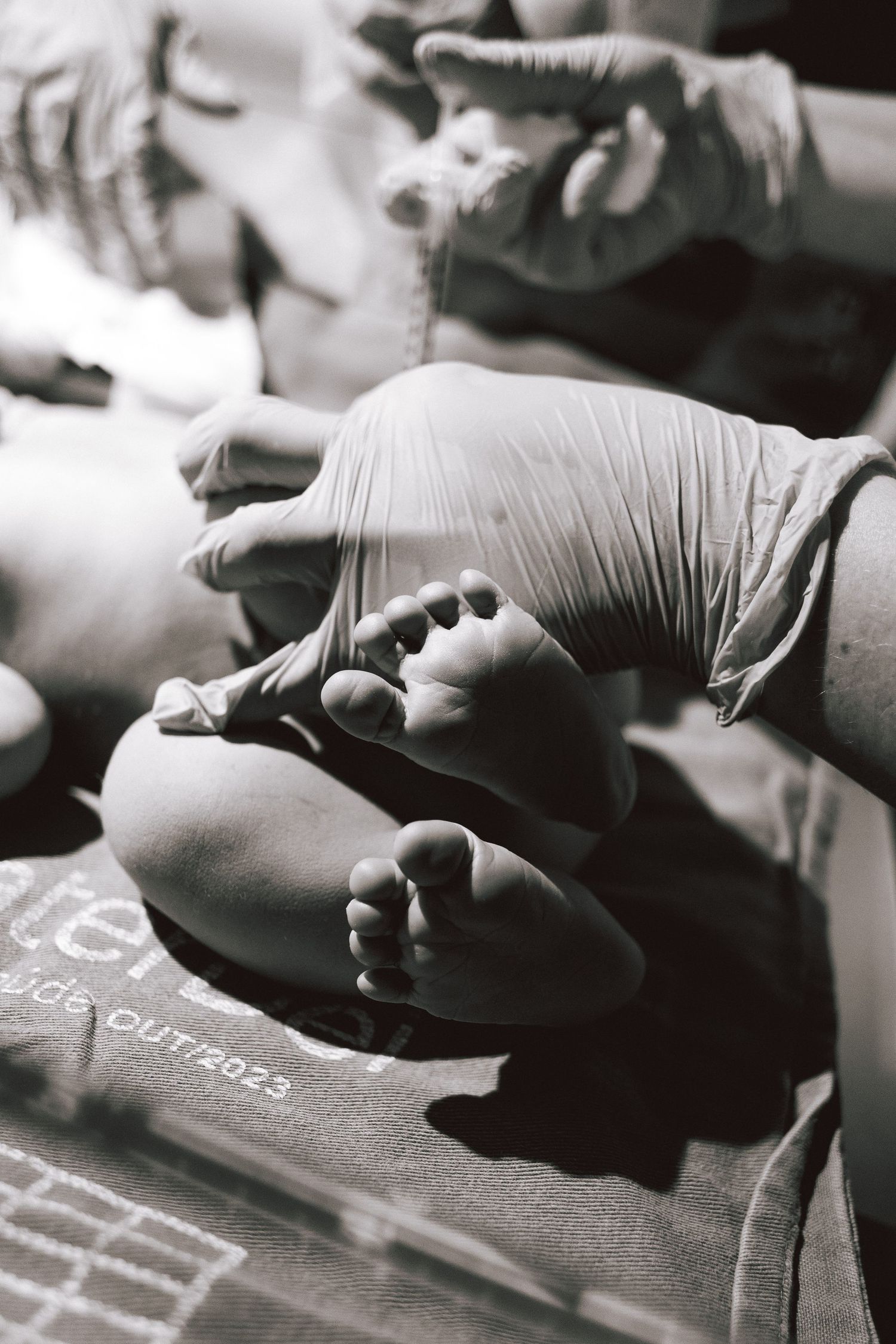 Black and white photo of a newborn baby's tiny feet held gently by gloved medical hands after birth.