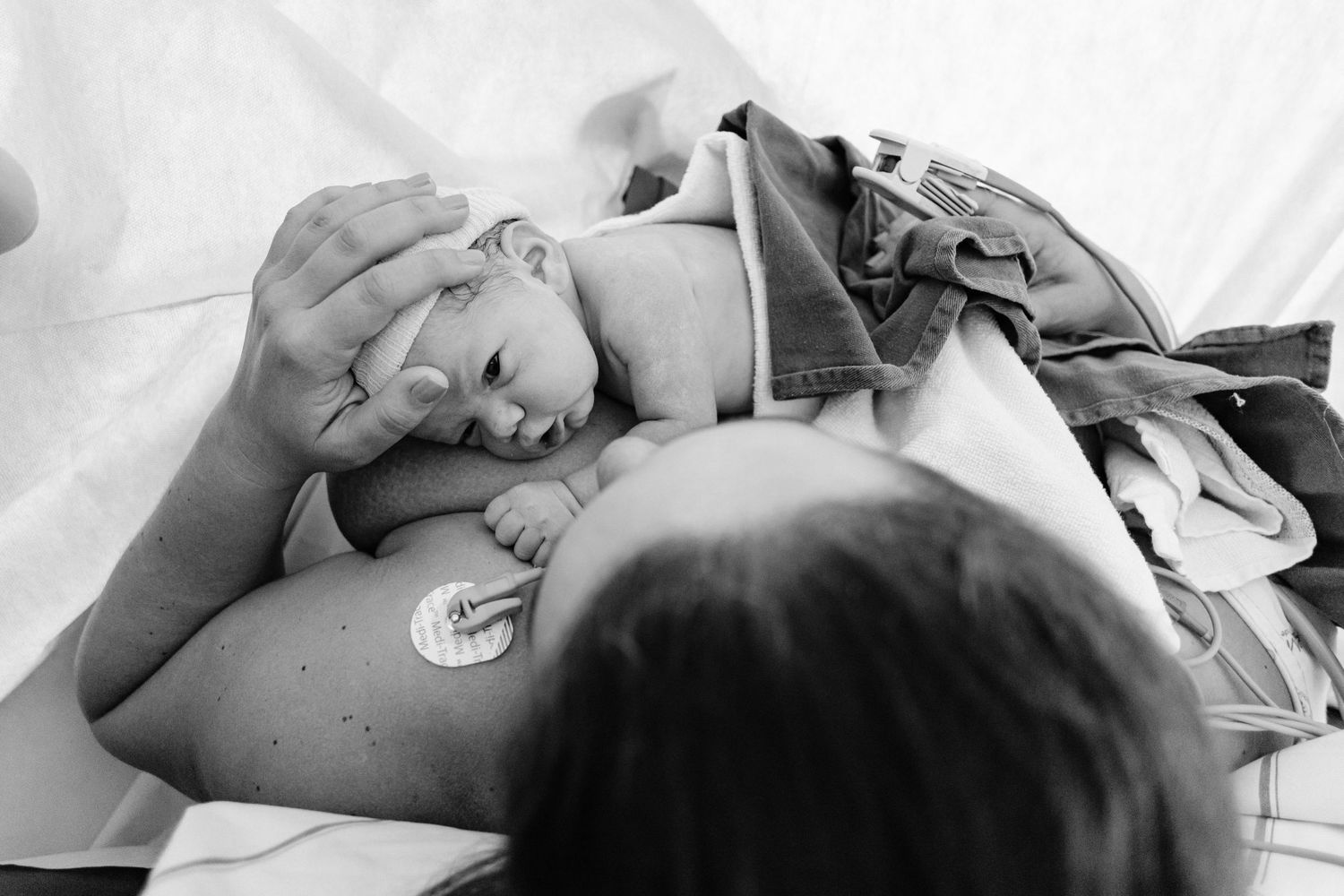 Black and white photo of a newborn resting on a soft surface in a hospital setting.