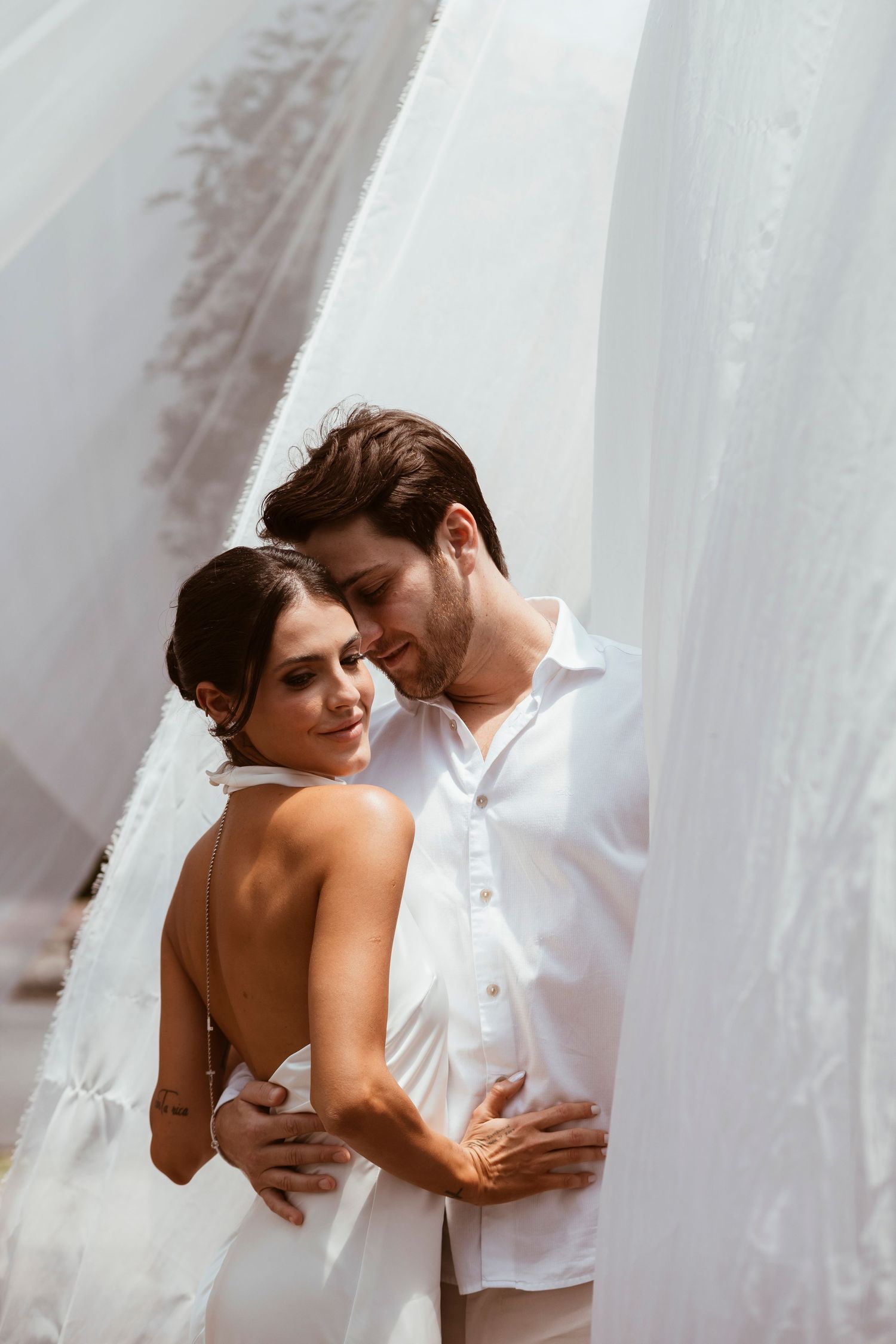 Intimate wedding portrait of couple sharing tender moment against white backdrop.