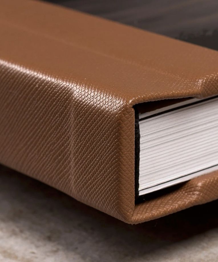 Close-up of a brown textured leather-bound notebook with white pages on a marble surface.