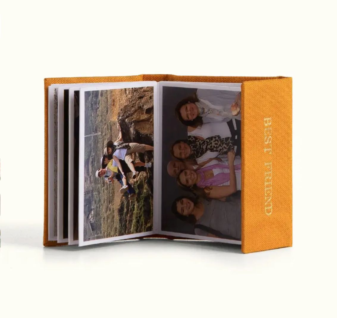Small orange hardcover photo book labeled Best Friends, open to show group photos of smiling friends inside.