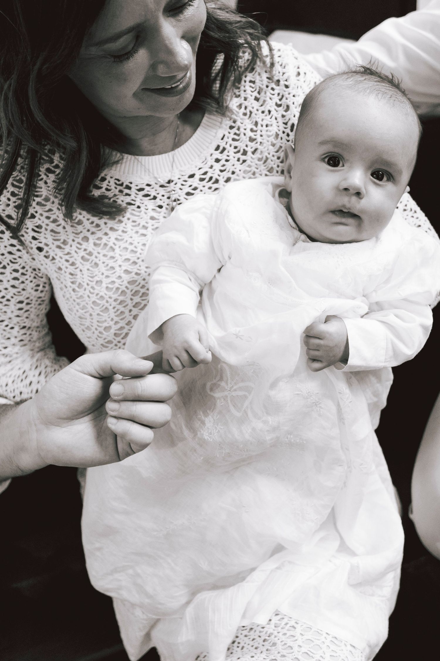 Black and white photo series showing a baby in white dress with lace details being held in someone's arms.
