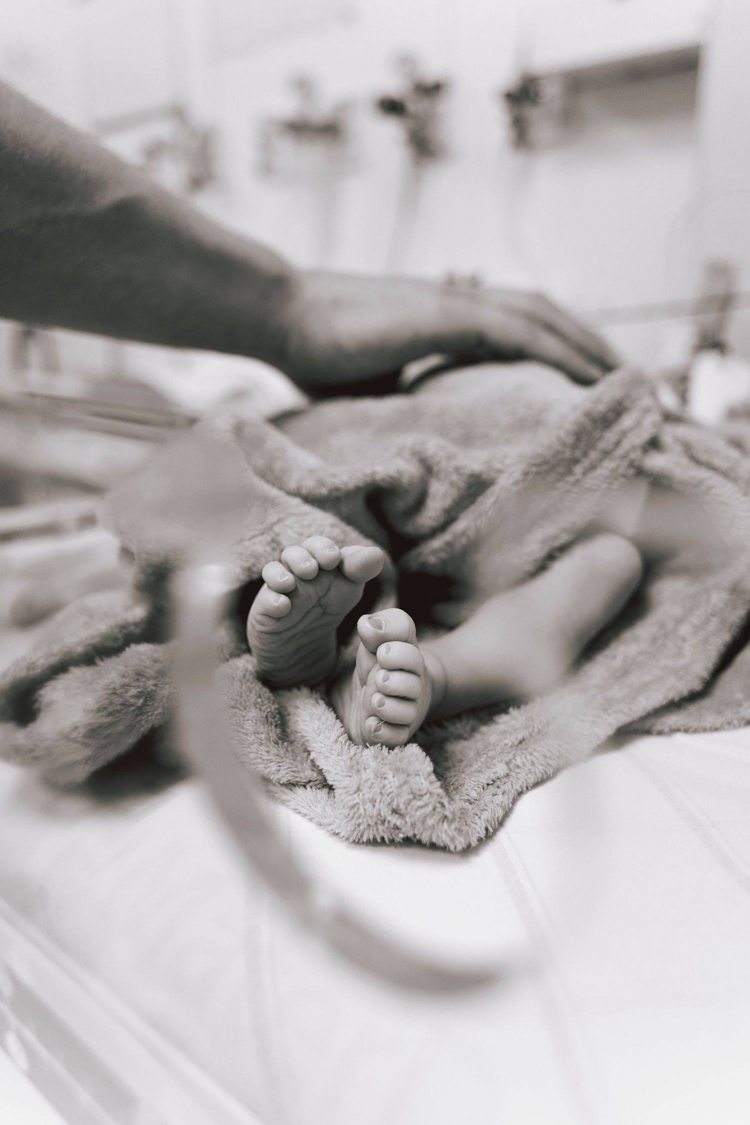 Black and white close-up image of tiny newborn feet wrapped in soft hospital blanket.