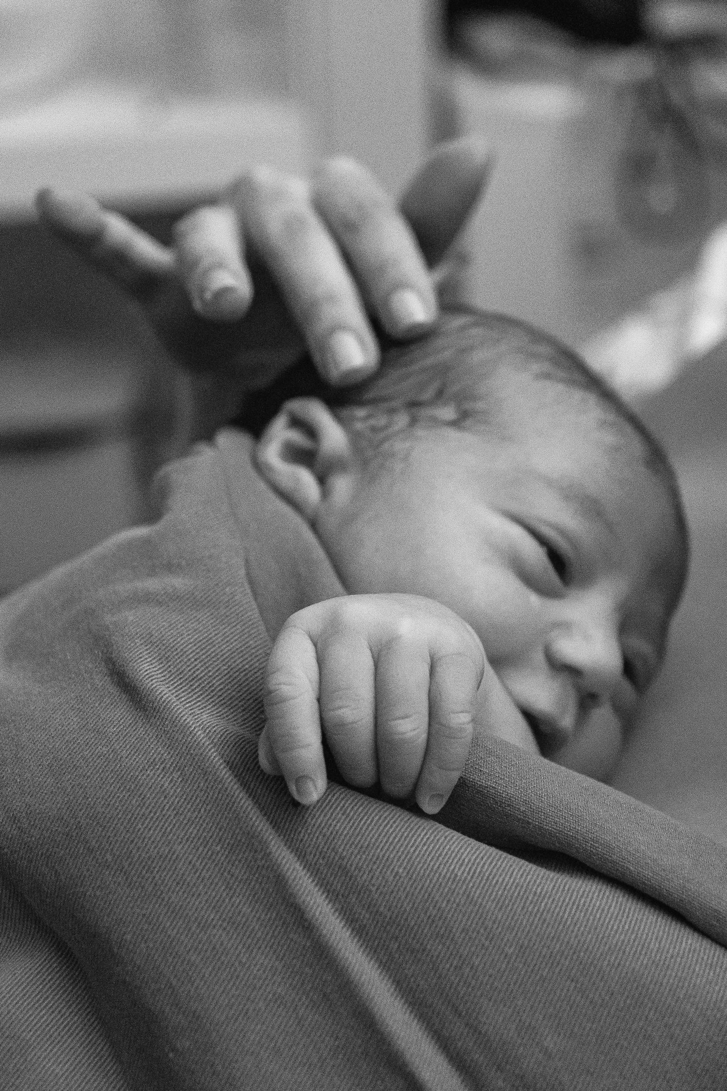 A newborn baby rests peacefully while a gentle hand provides comfort and care.