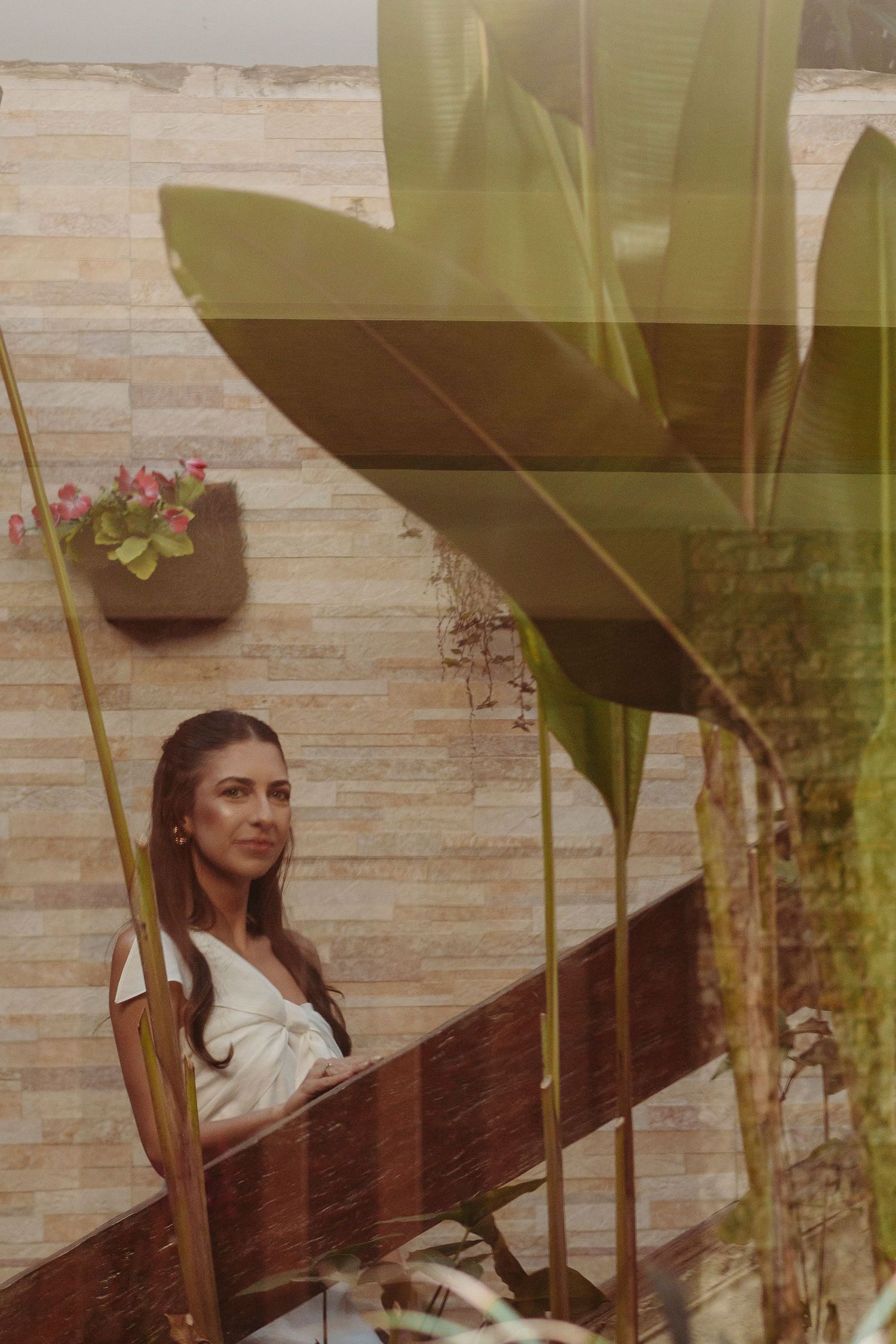 A woman in white sits on wooden stairs surrounded by tropical plants.