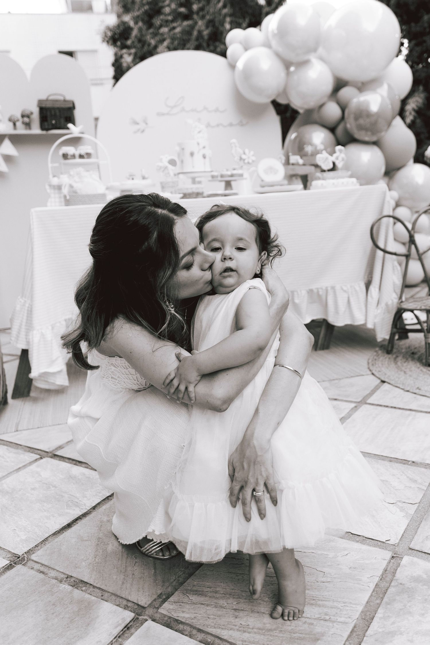 A tender black and white moment captured at an outdoor celebration with balloon decorations.