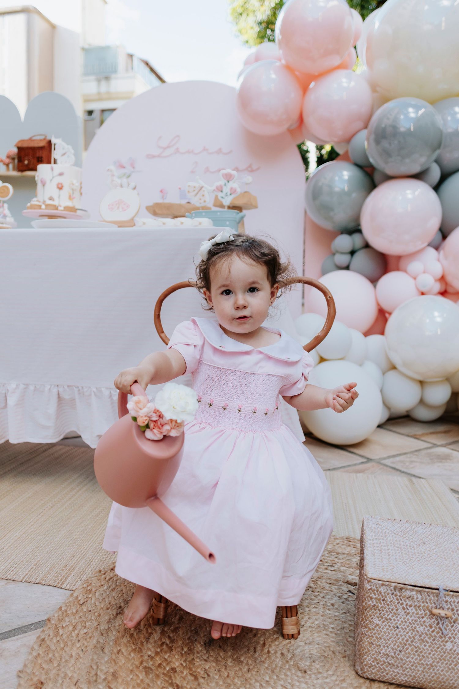 A child in a pink dress poses with balloons at a decorated party setting.