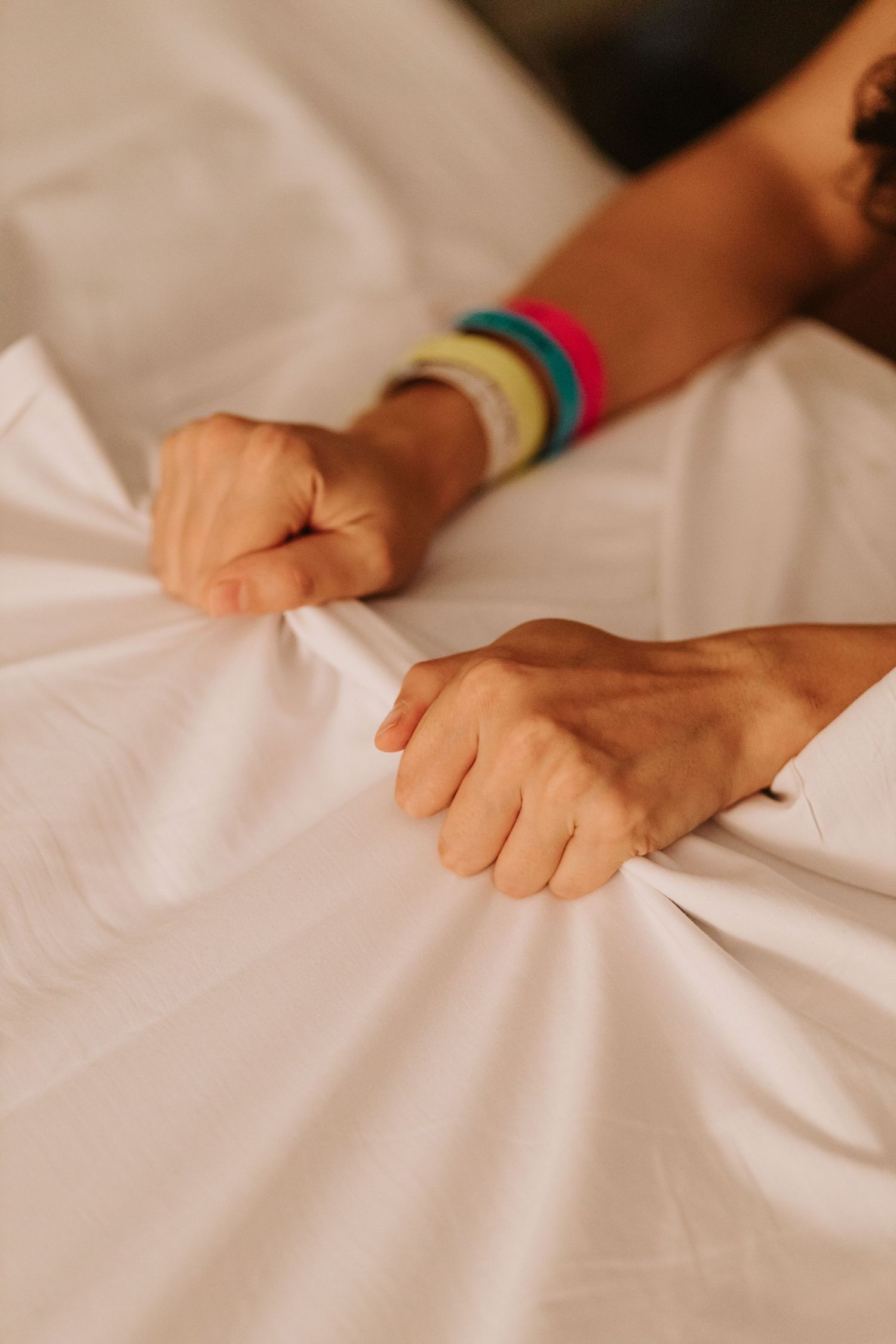 Hands gripping white hospital bedding with colorful wristbands visible.