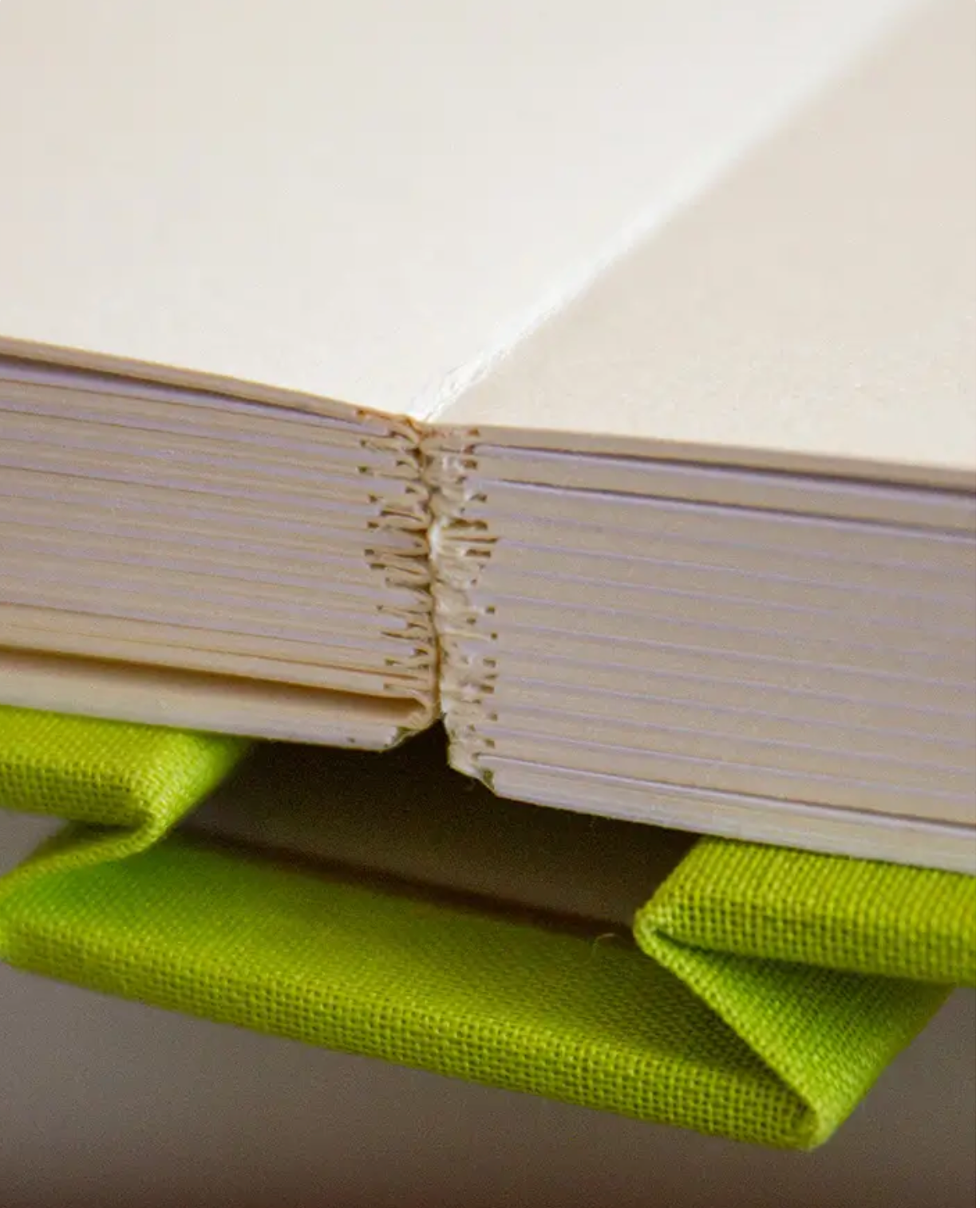 Close-up of a hand-sewn book binding with yellow thread stitching and a lime green fabric cover spine.