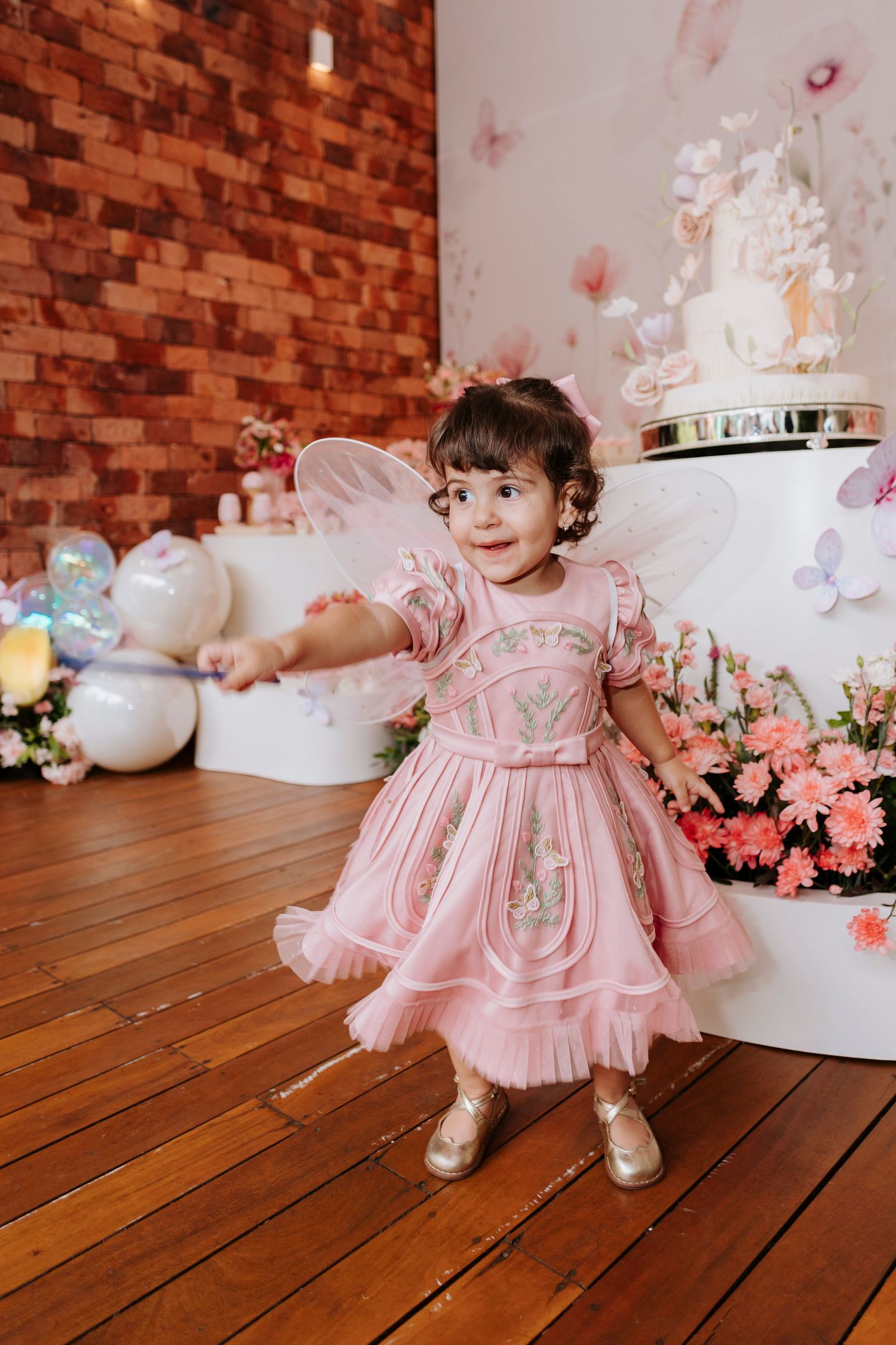 Little girl in pink princess dress twirling at party with floral decorations.