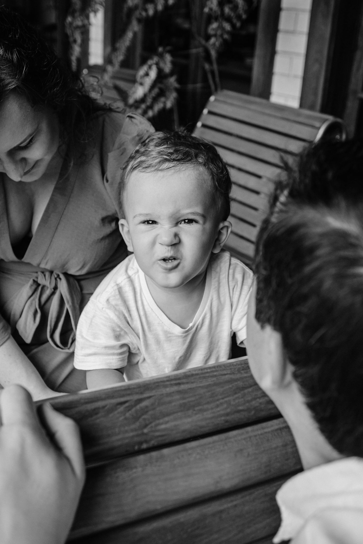 Black and white photo of a playful family moment on a wooden bench outdoors.