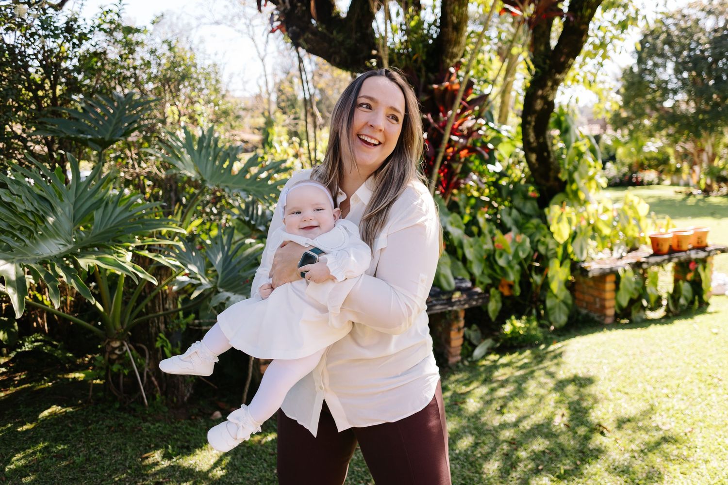 A mother and baby share joyful moments together while playing in a sunlit garden setting.