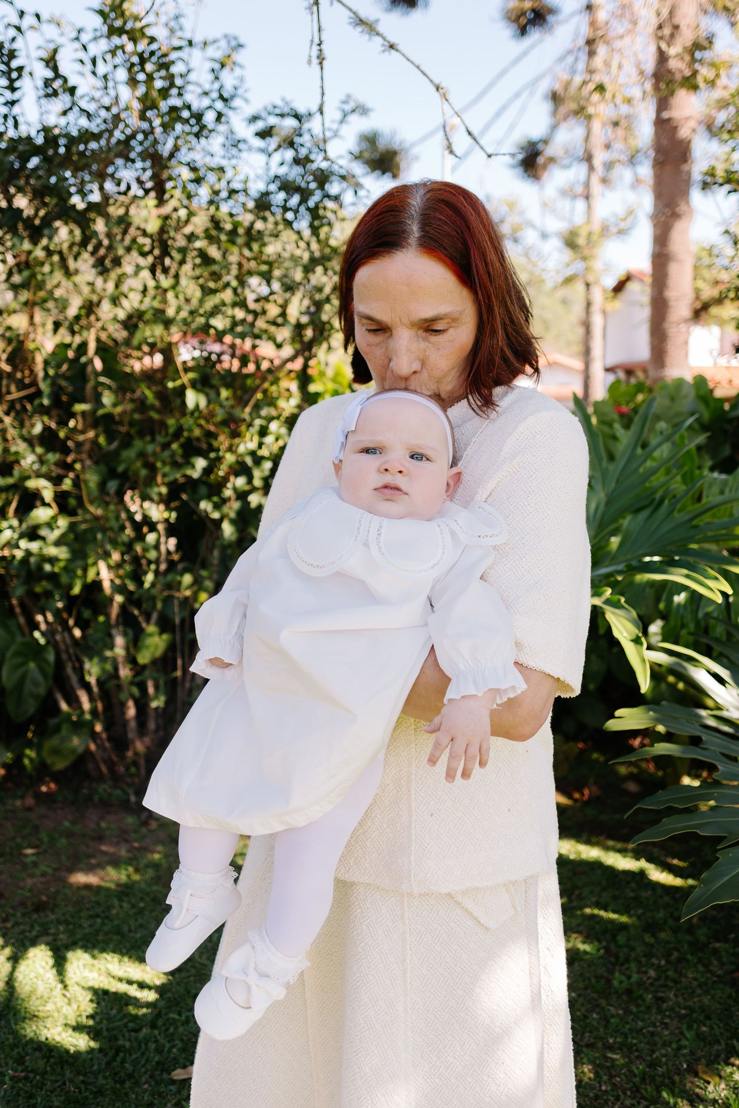 Parent and baby in white outfits share sweet moments together in a sunny garden setting.
