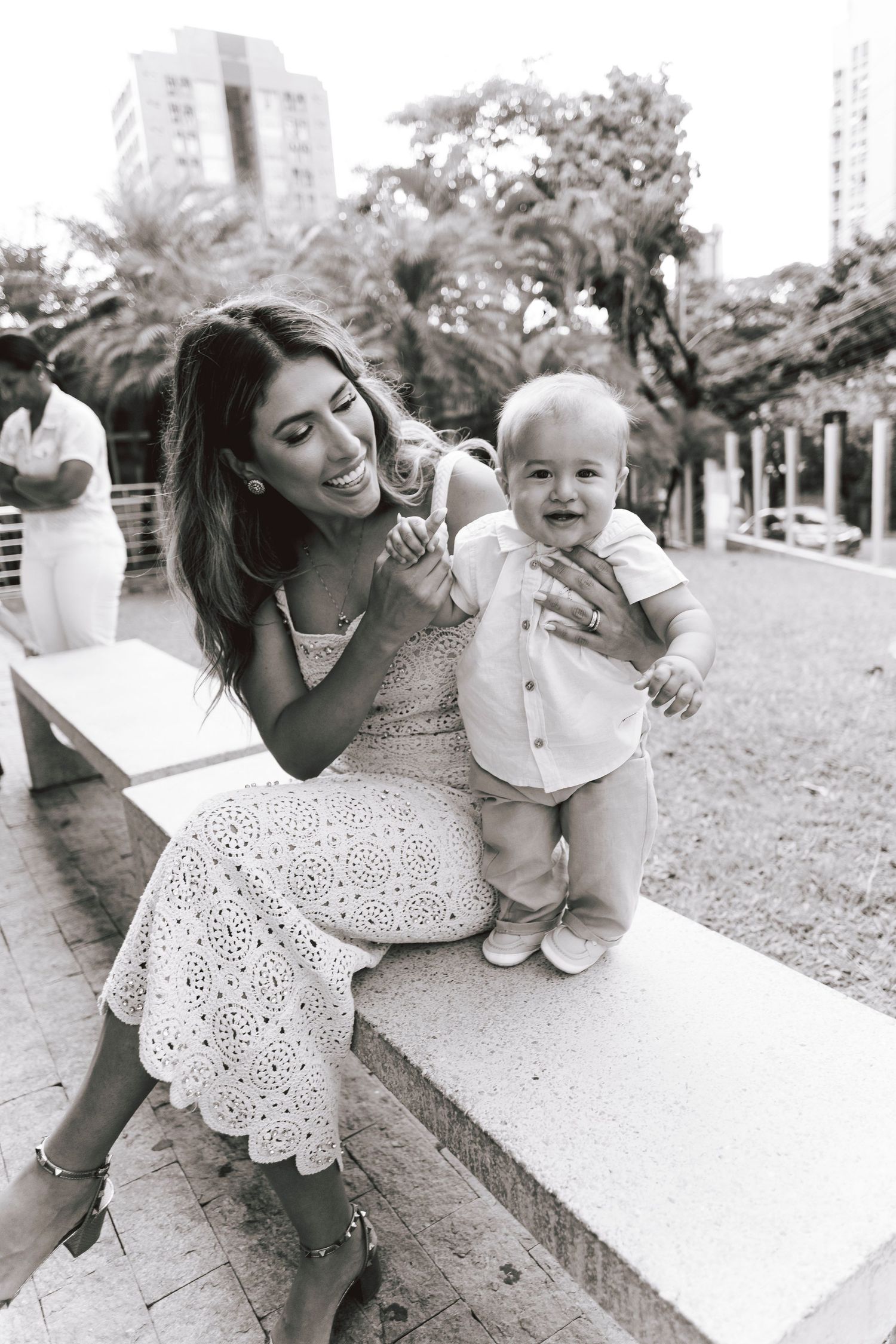 A tender moment between a parent and baby in a garden setting wearing white eyelet dress and casual attire.