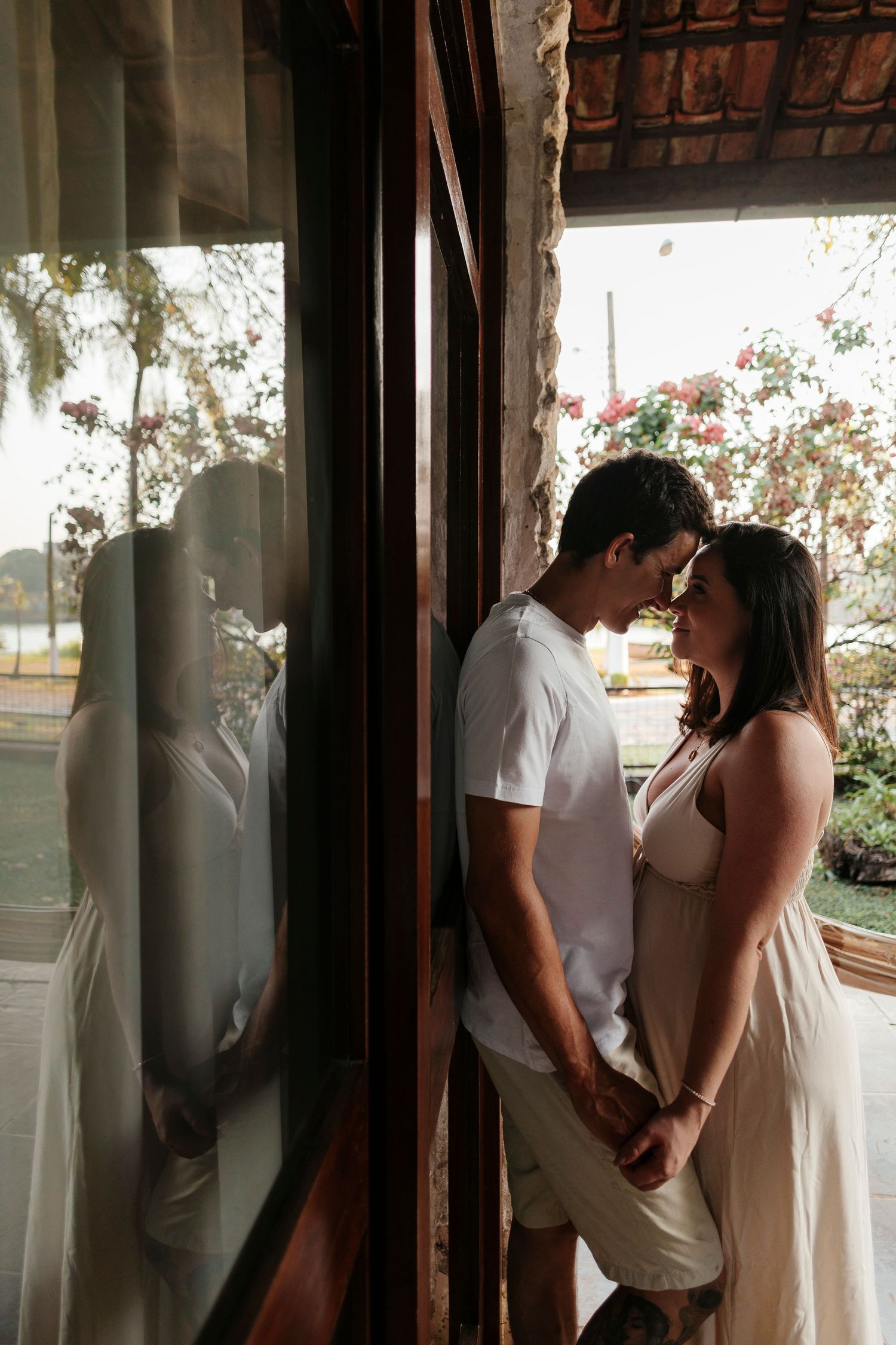 Romantic maternity photo of couple standing by window with natural light.