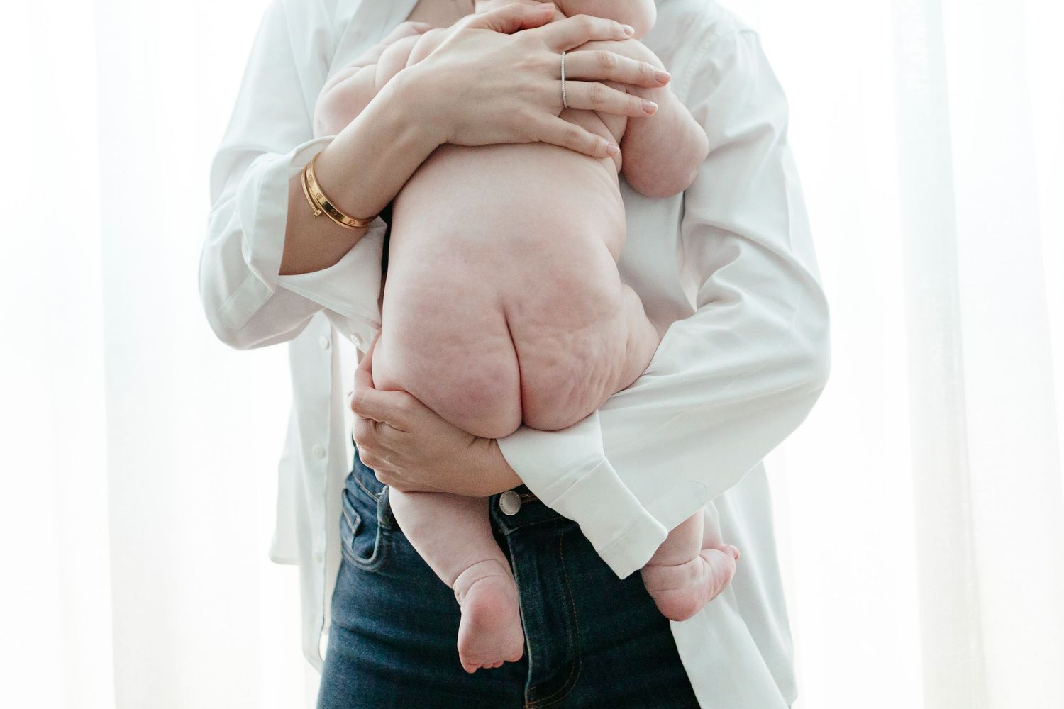 Close-up of parent holding baby's bare belly in white shirt and jeans.