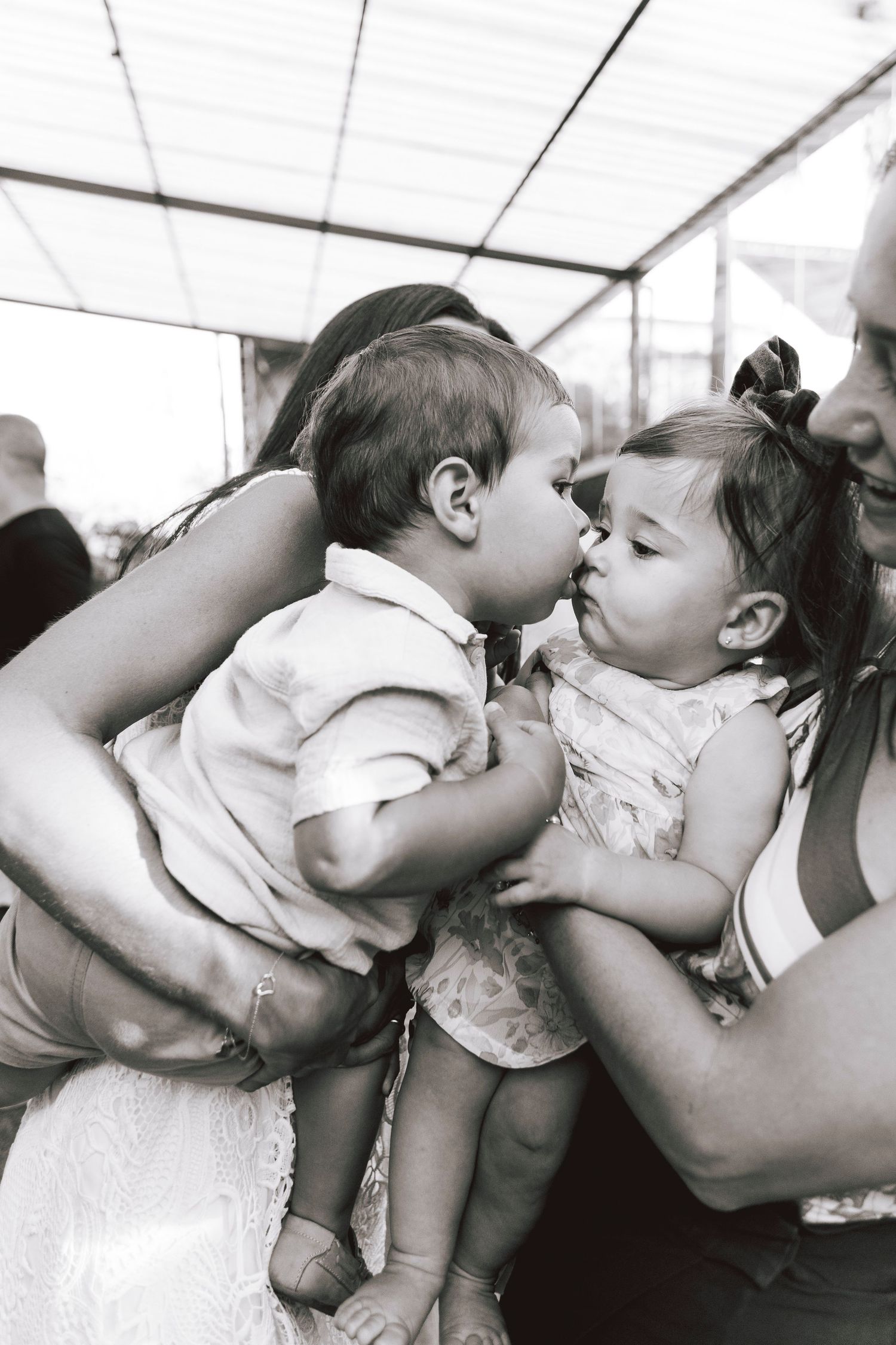 Two small children share a sweet moment while being held at a family event.