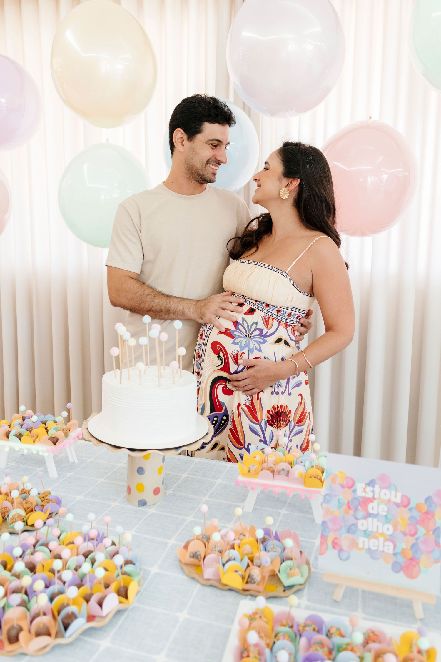 A couple shares an intimate moment at a dessert table decorated with colorful cake pops and pastel balloons.