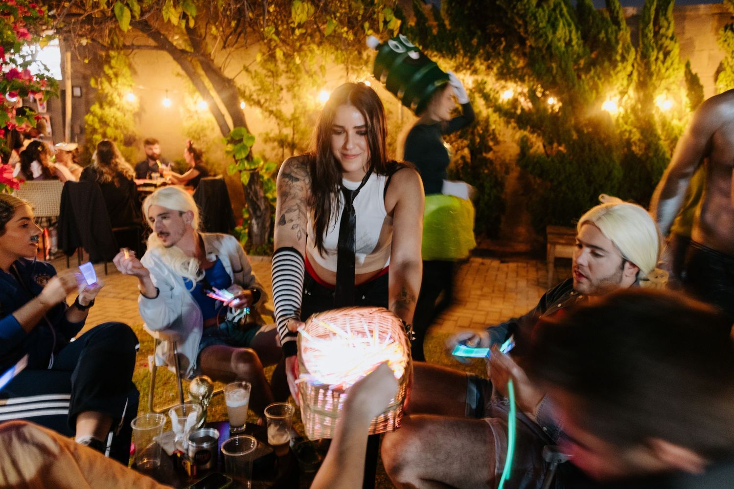 Guests gather at an outdoor evening party with warm lighting and trees creating an intimate atmosphere.