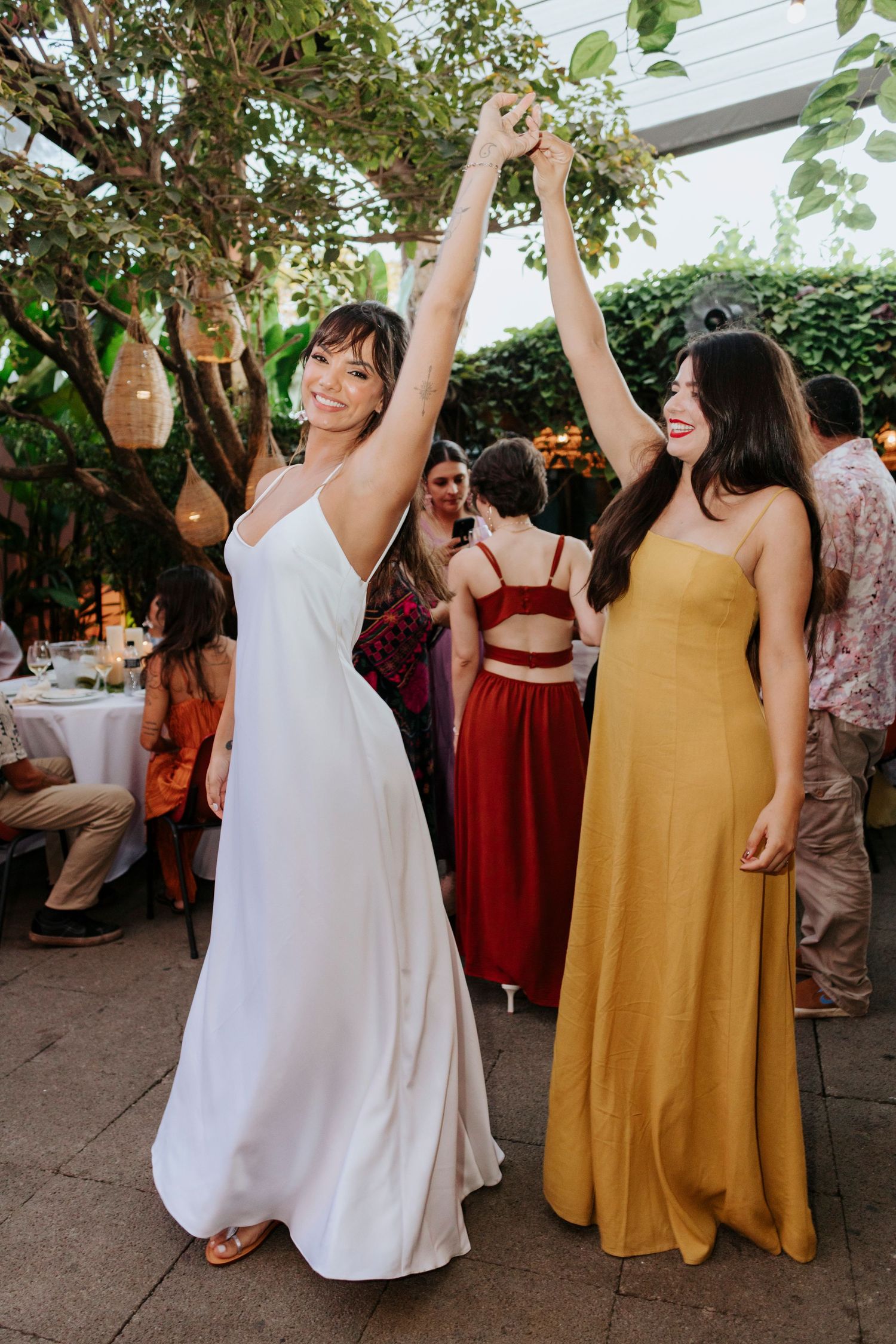 Wedding guests in elegant dresses dancing at outdoor reception with string lights.