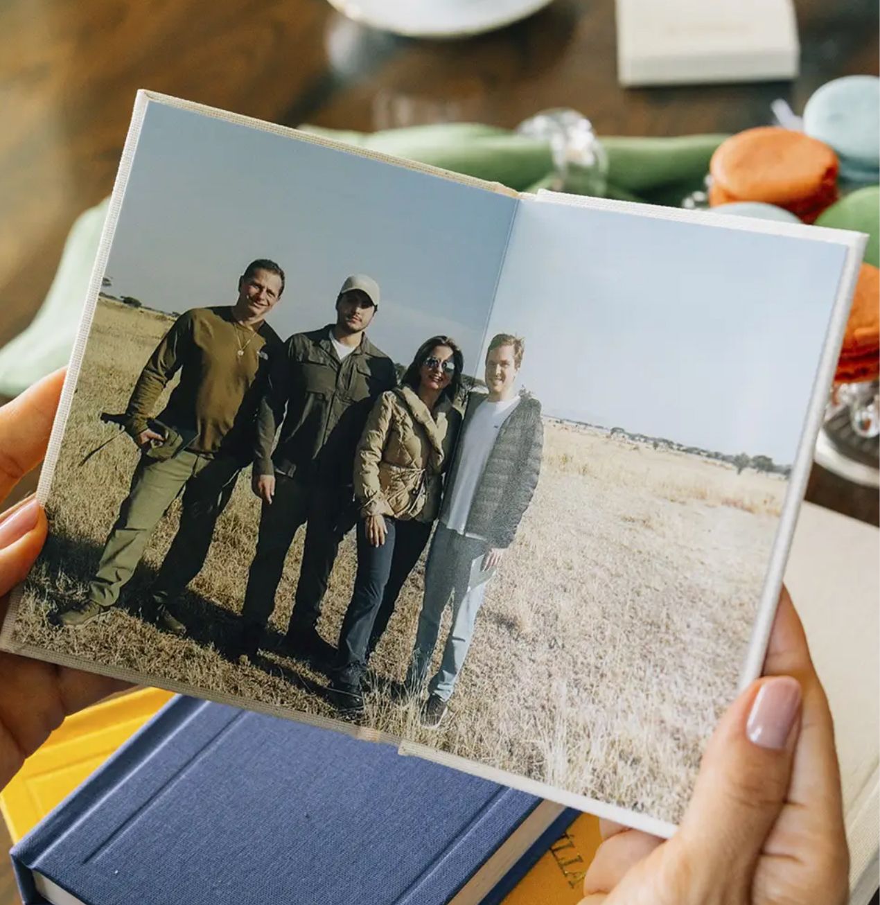 Hands holding a small photo book open to a picture of four people posing together in an open field.