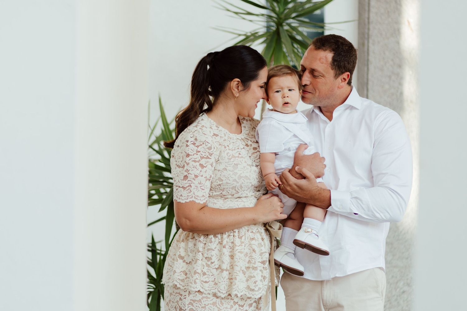 Family wearing white outfits poses together in front of tropical greenery for a photo session.