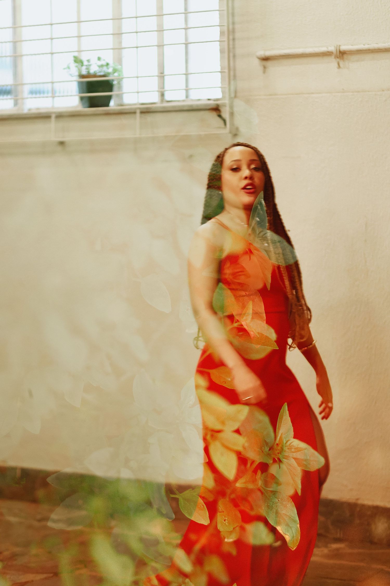 Woman in red floral dress posing gracefully indoors near a window with soft natural light.