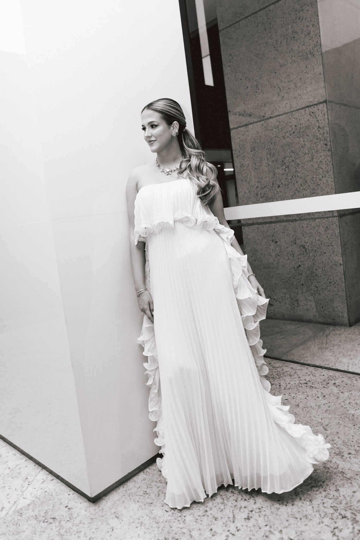 Elegant white pleated wedding dress with ruffled details shown in a series of artistic outdoor poses.