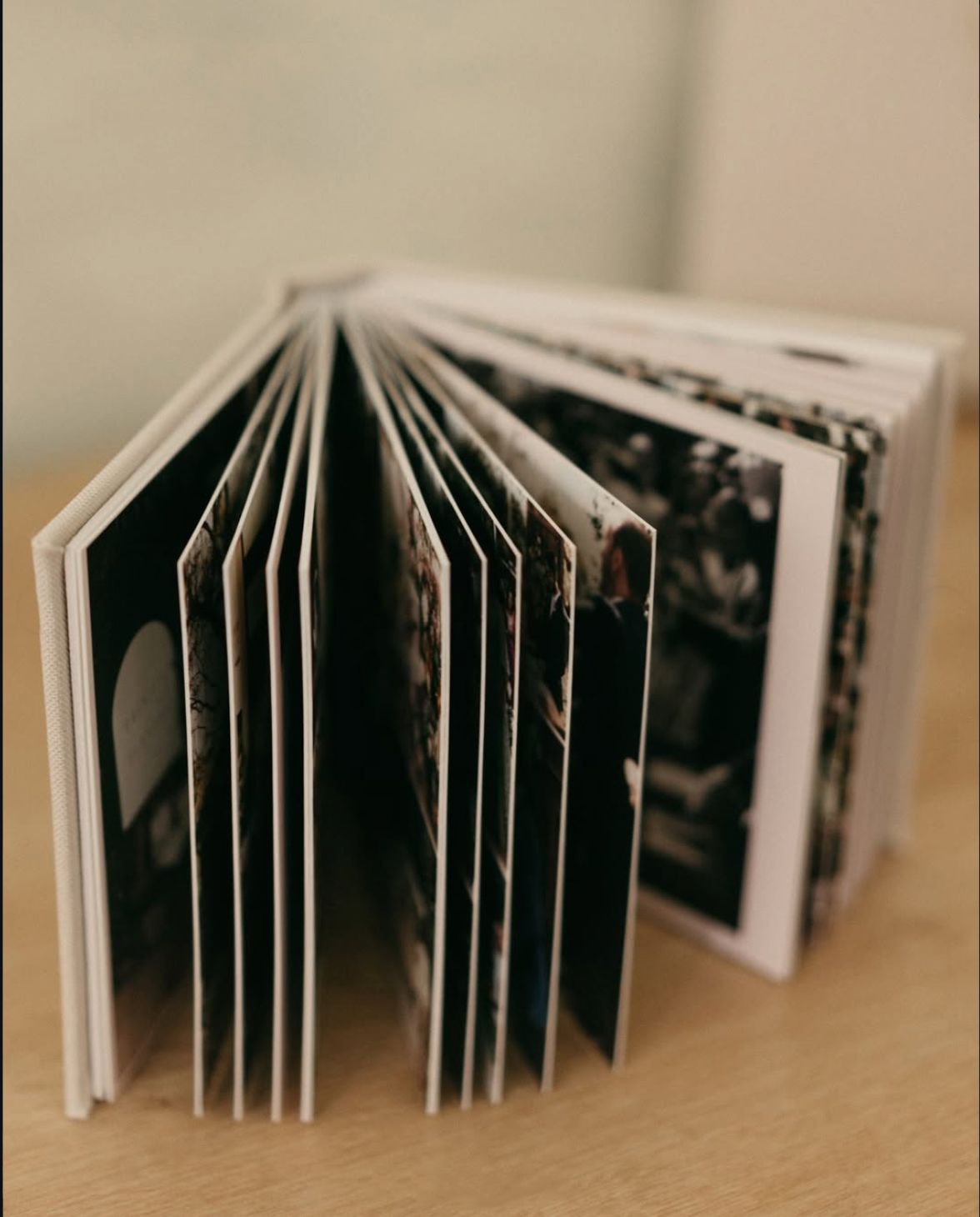 Open photo book with black and white images fanned out on a wooden table, showcasing printed photography pages.