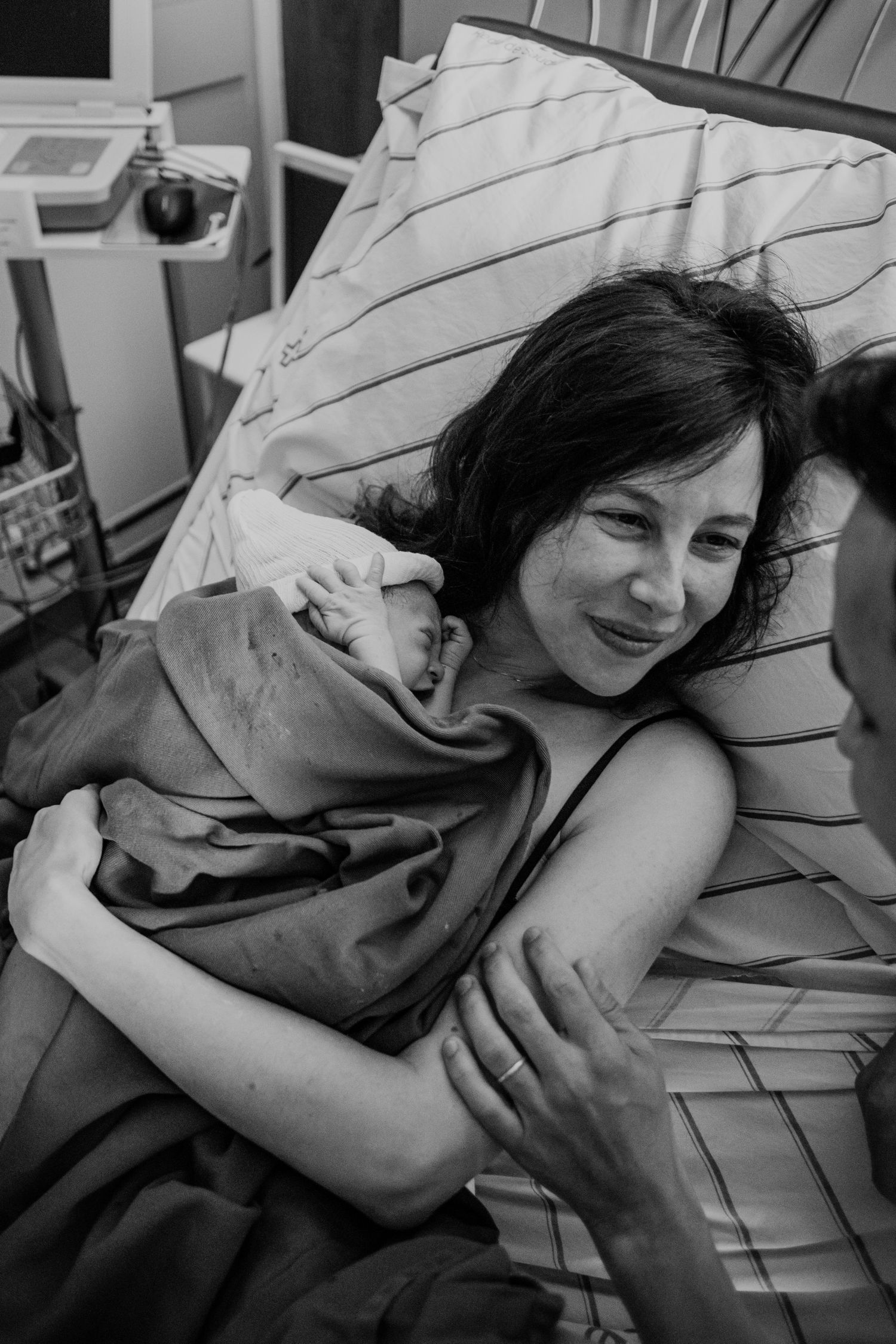 Black and white photograph capturing emotional moments after childbirth in hospital room.