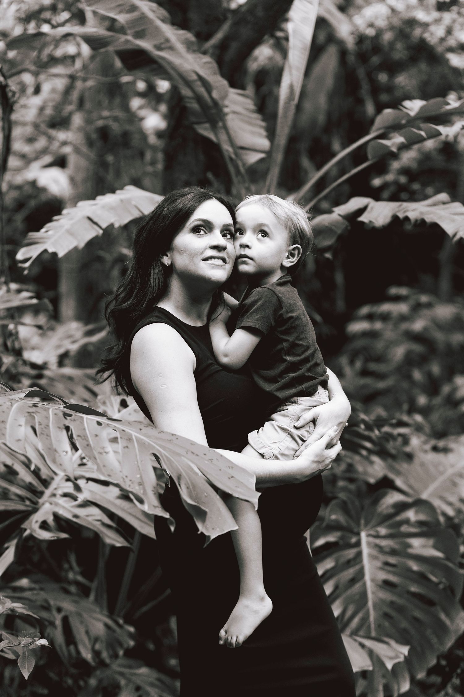 Mother and child share a tender moment amongst tropical foliage in black and white portrait.