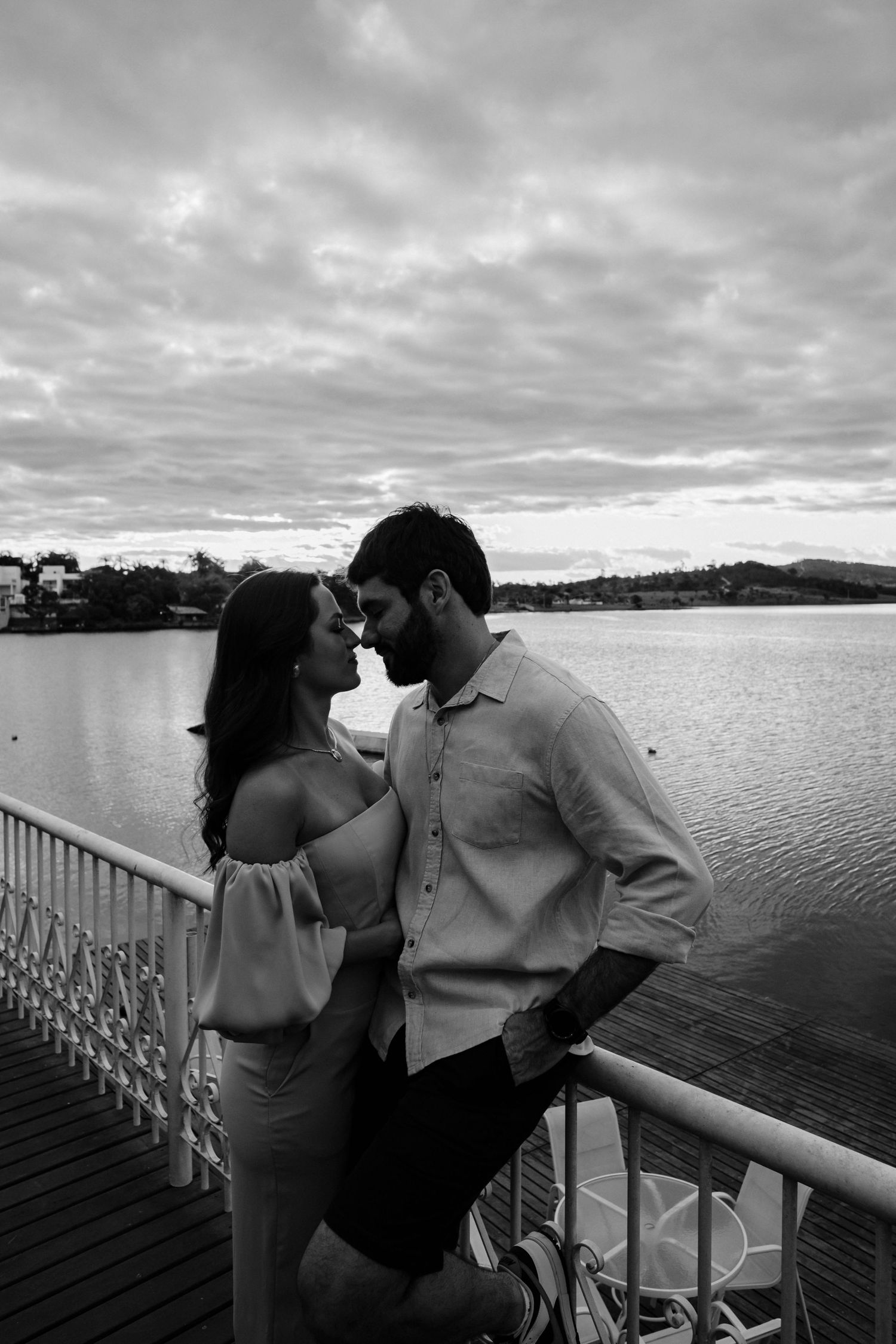 Romantic couple sharing an intimate moment at sunset on a lakeside dock with cloudy skies.