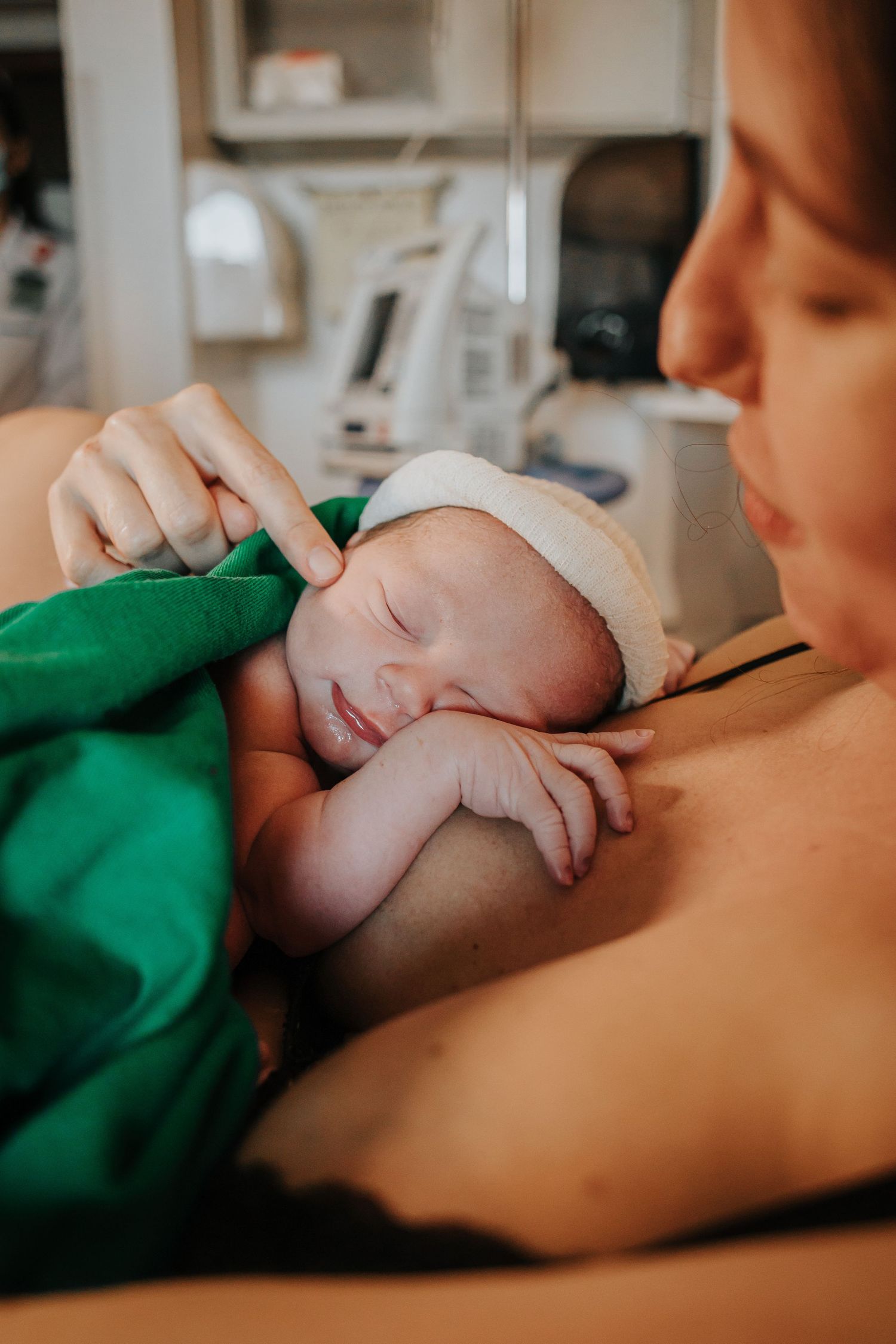 Newborn baby wrapped in green blanket sleeping peacefully on parent's chest.