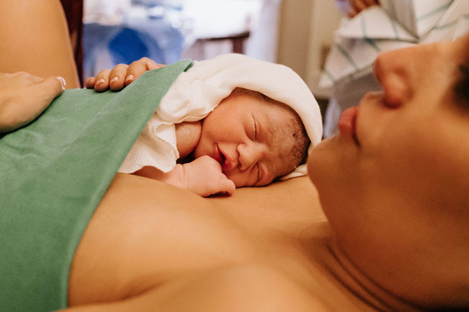 A newborn baby rests on mother's chest immediately after birth in the delivery room.