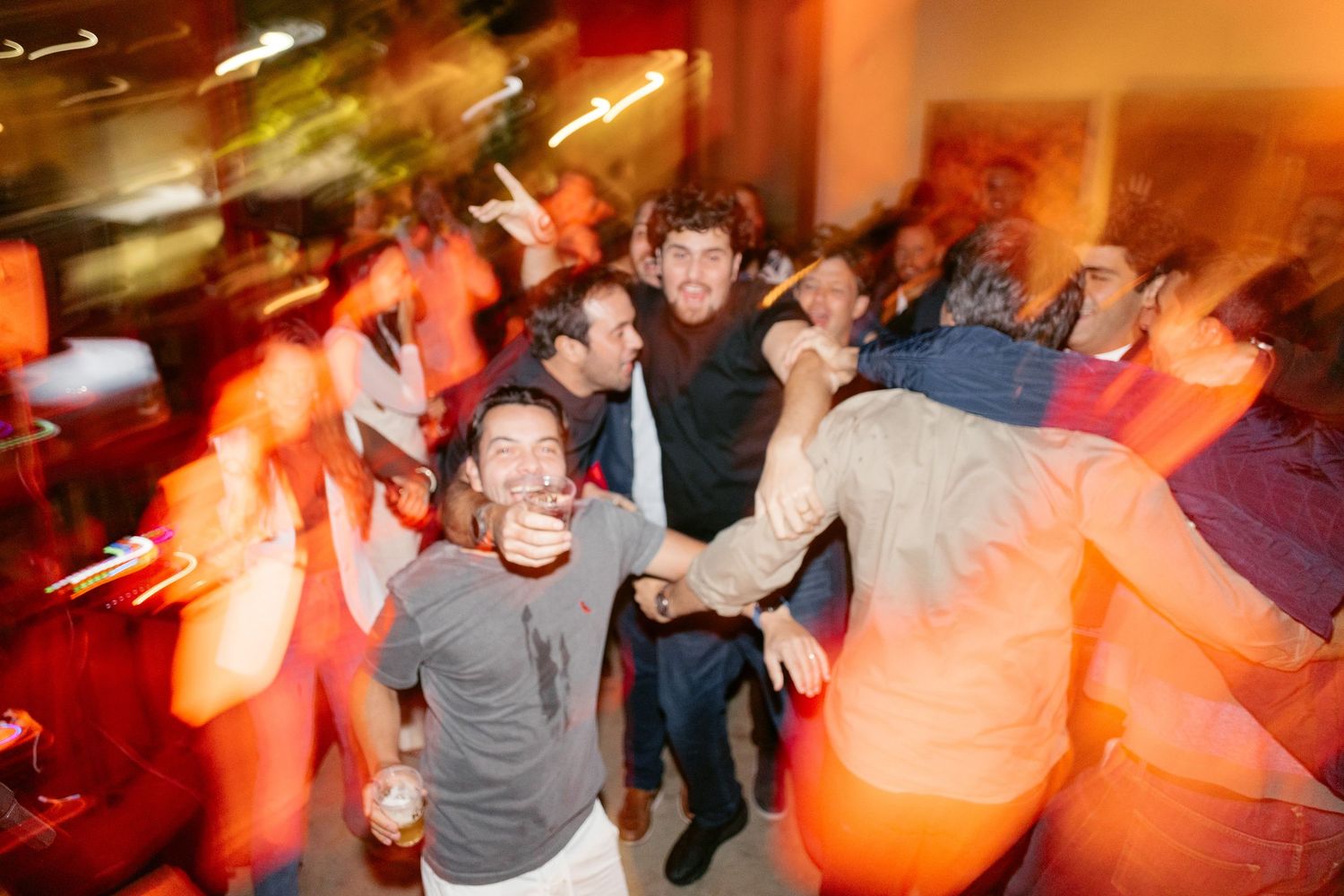 People dancing and celebrating at a lively party with orange and red lighting effects.