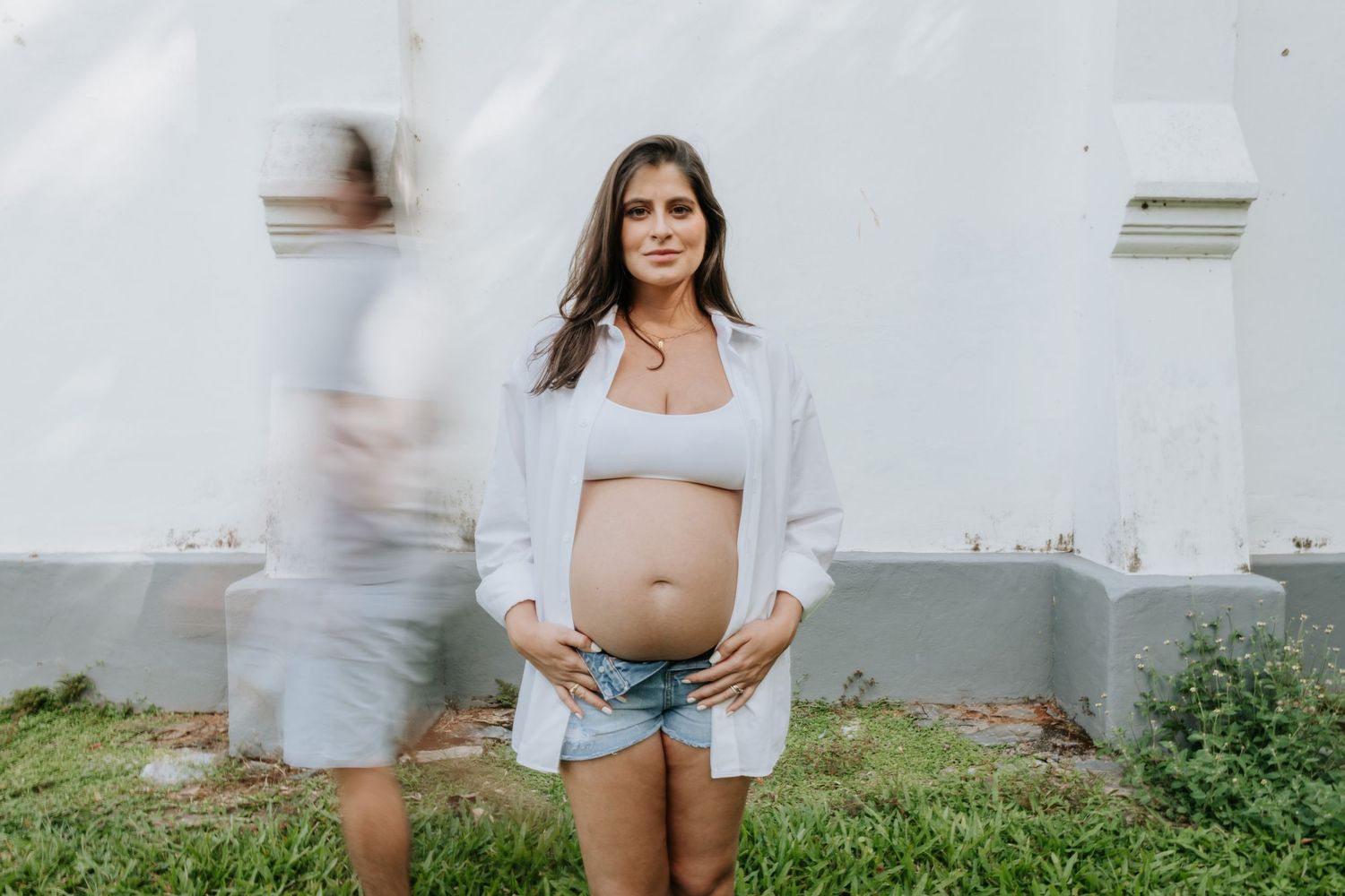 A woman wearing white shorts and a white crop top poses outdoors against a light-colored wall.