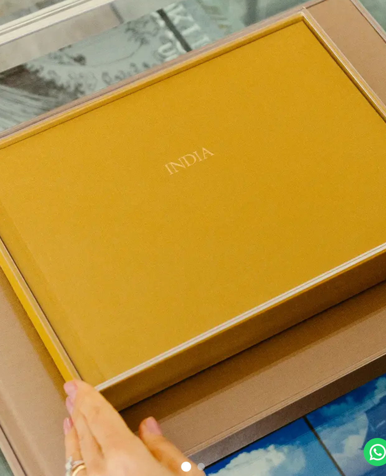 A hand holding a mustard yellow leather-bound photo book labeled INDIA in a matching gift box.