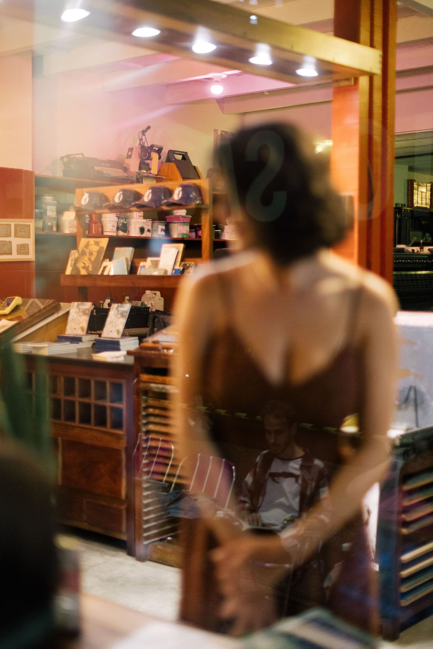 Woman in brown dress browsing a warm-lit boutique shop with wooden shelves displaying books and accessories.