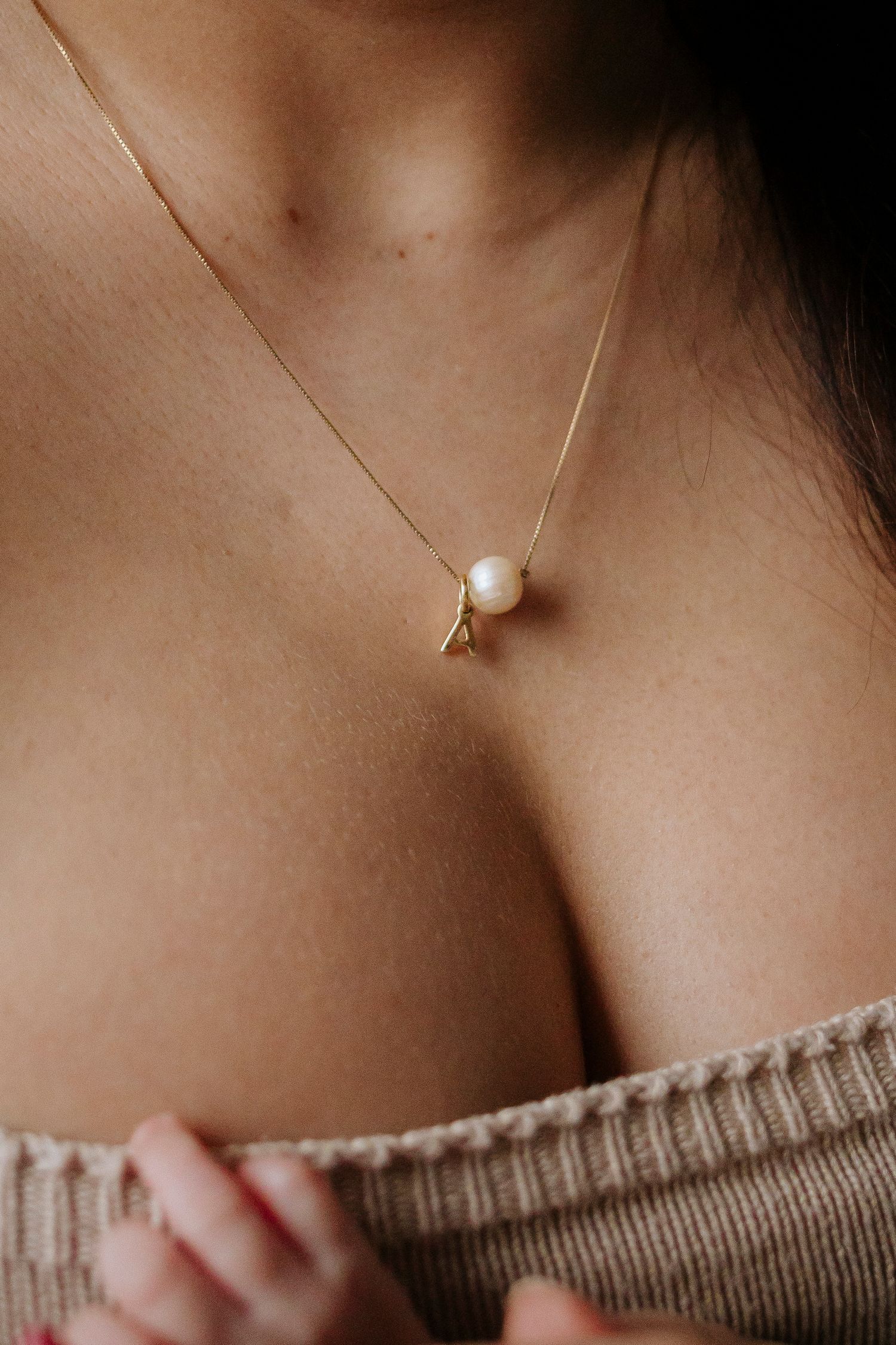 Delicate gold and pearl pendant necklace worn with a knit sweater.
