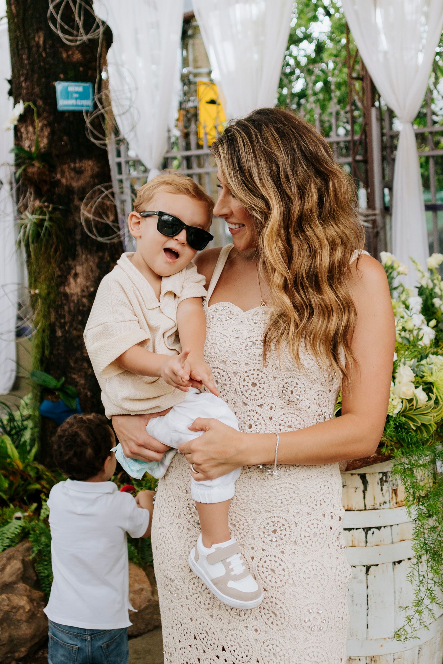 Family moment outdoors with white decor where child wears sunglasses while being held.