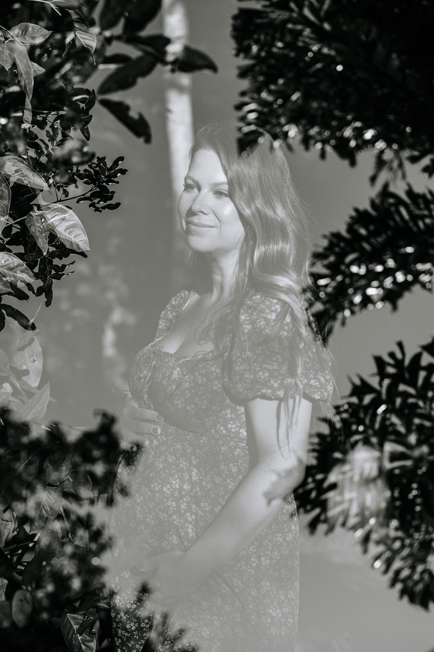 Dreamy black and white portrait of expectant mother among garden foliage.