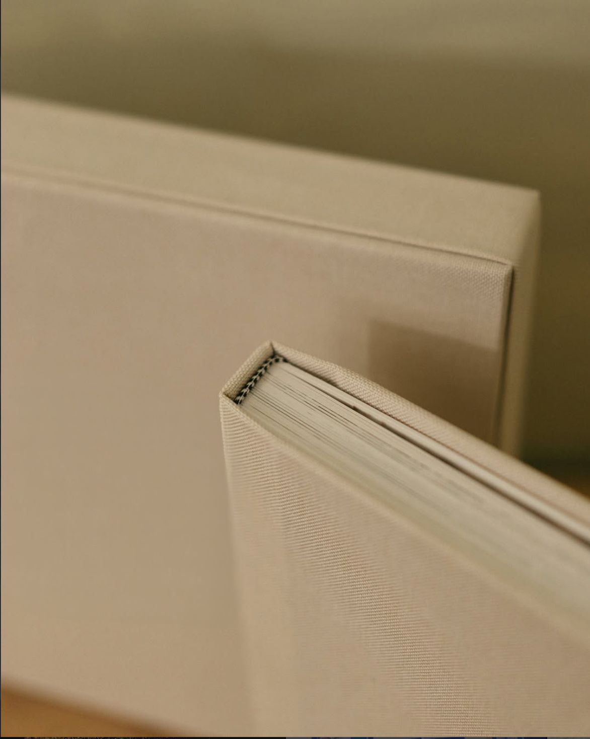 Close-up of two beige linen-covered hardcover books stacked together, showing spiral binding detail.